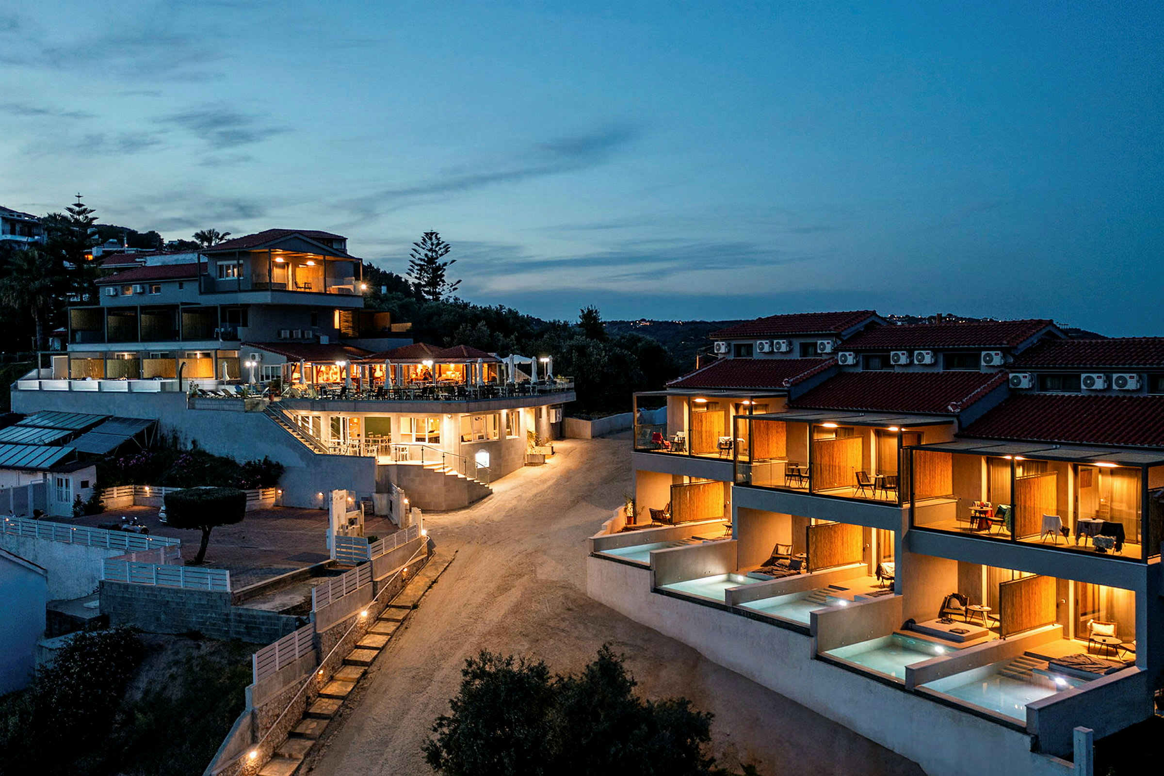 Bild av ett hotell med upplysta byggnader och privata poolområden under en kvällshimmel. (AI-genererad text)