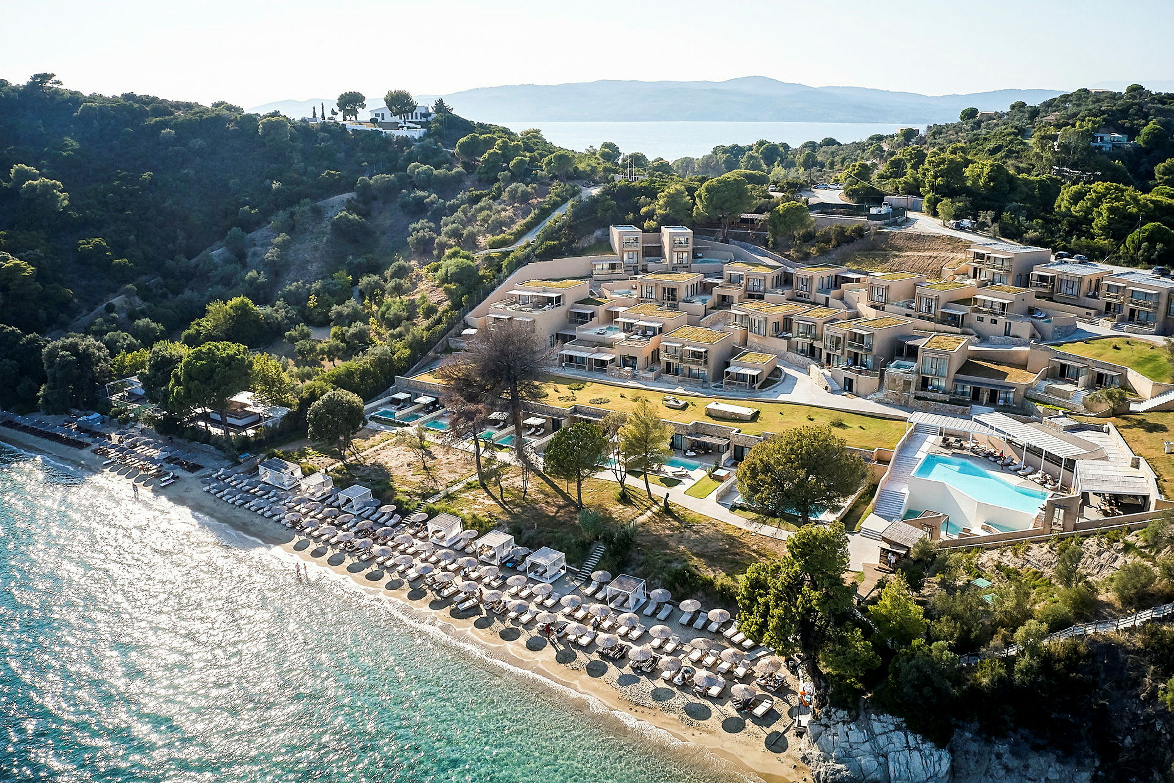 Flygfoto av resort med pool, strand med parasoller och solstolar, samt omgivande grönska. (AI-genererad text)