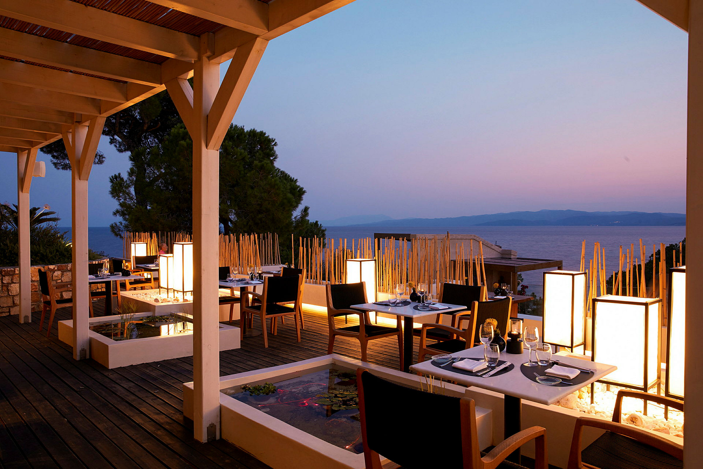 En restaurangterrass med bord och stolar vid solnedgången, havet i bakgrunden. (AI-genererad text)