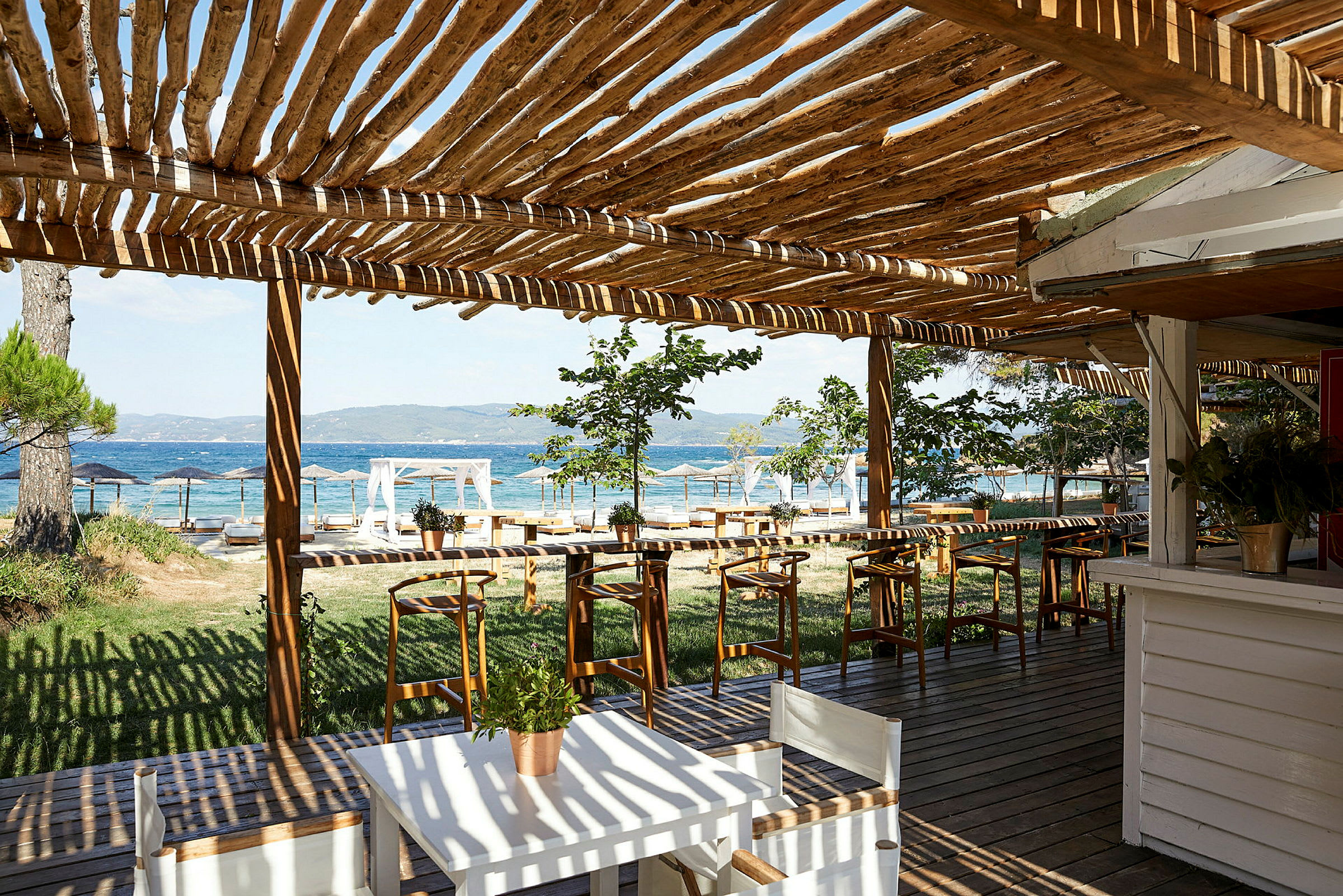 En uteplats med träpergola, bord och stolar, och utsikt över havet. (AI-genererad text)