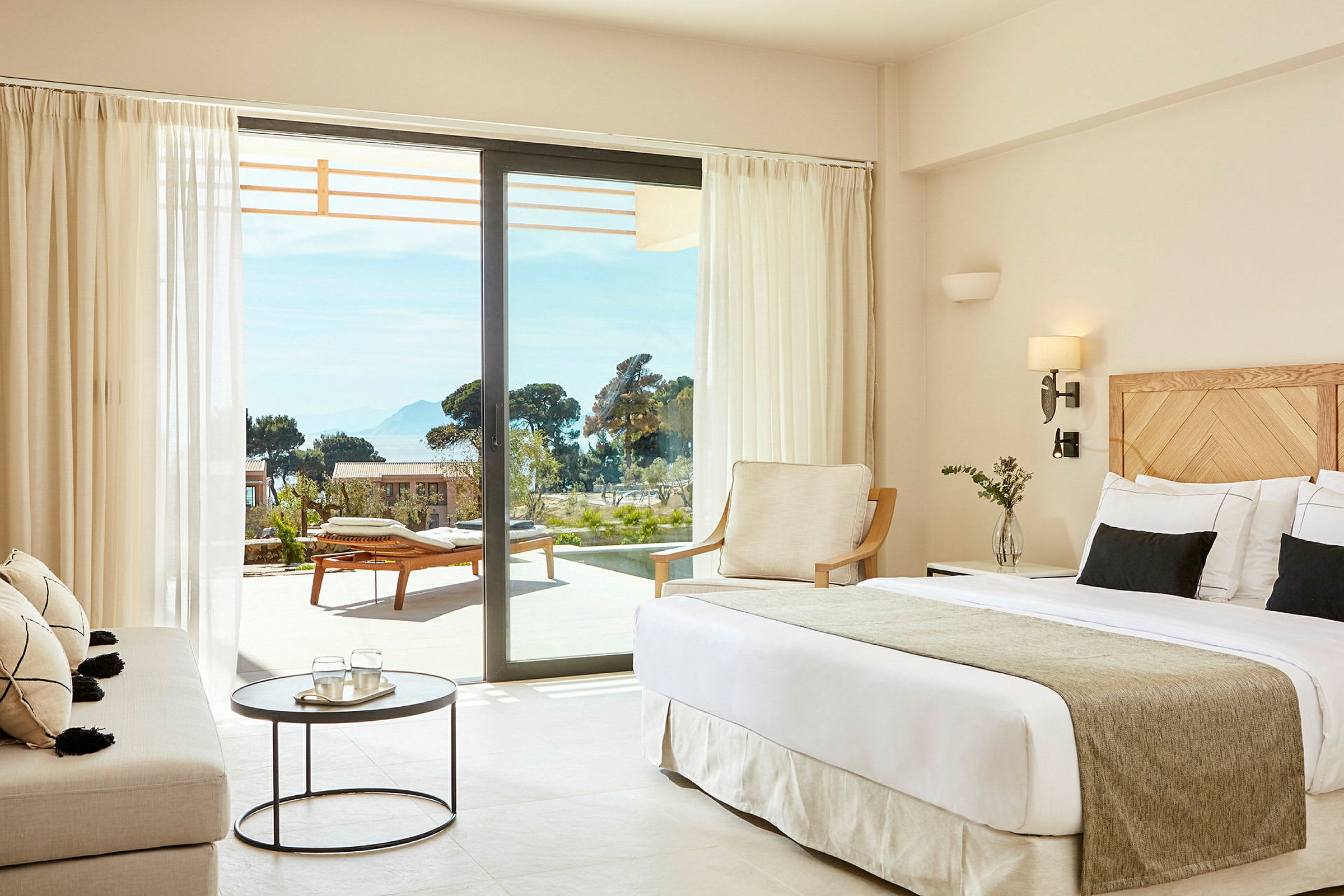 Ett hotellrum med modern inredning och utsikt mot en terrass med solstolar. (AI-genererad text)