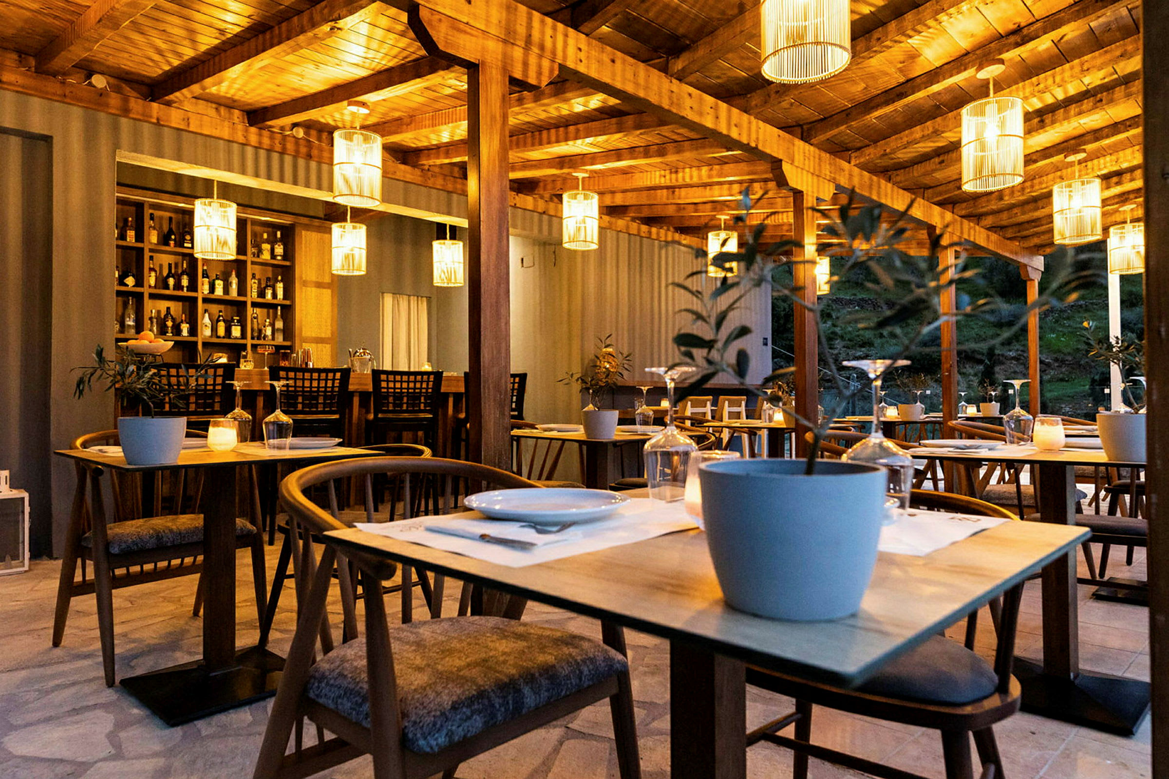En utomhusrestaurang med träbord och stolar, dekorerad med hängande lampskärmar och krukväxter. (AI-genererad text)