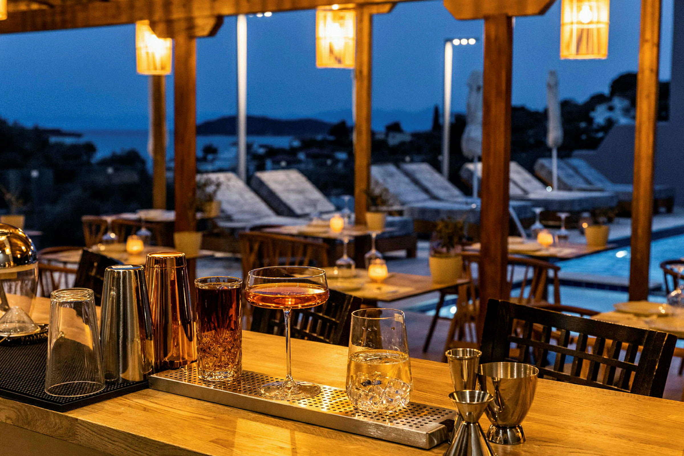 Cocktailglas och drinkar står på en bardisk vid en kvällsbelyst terrass. (AI-genererad text)
