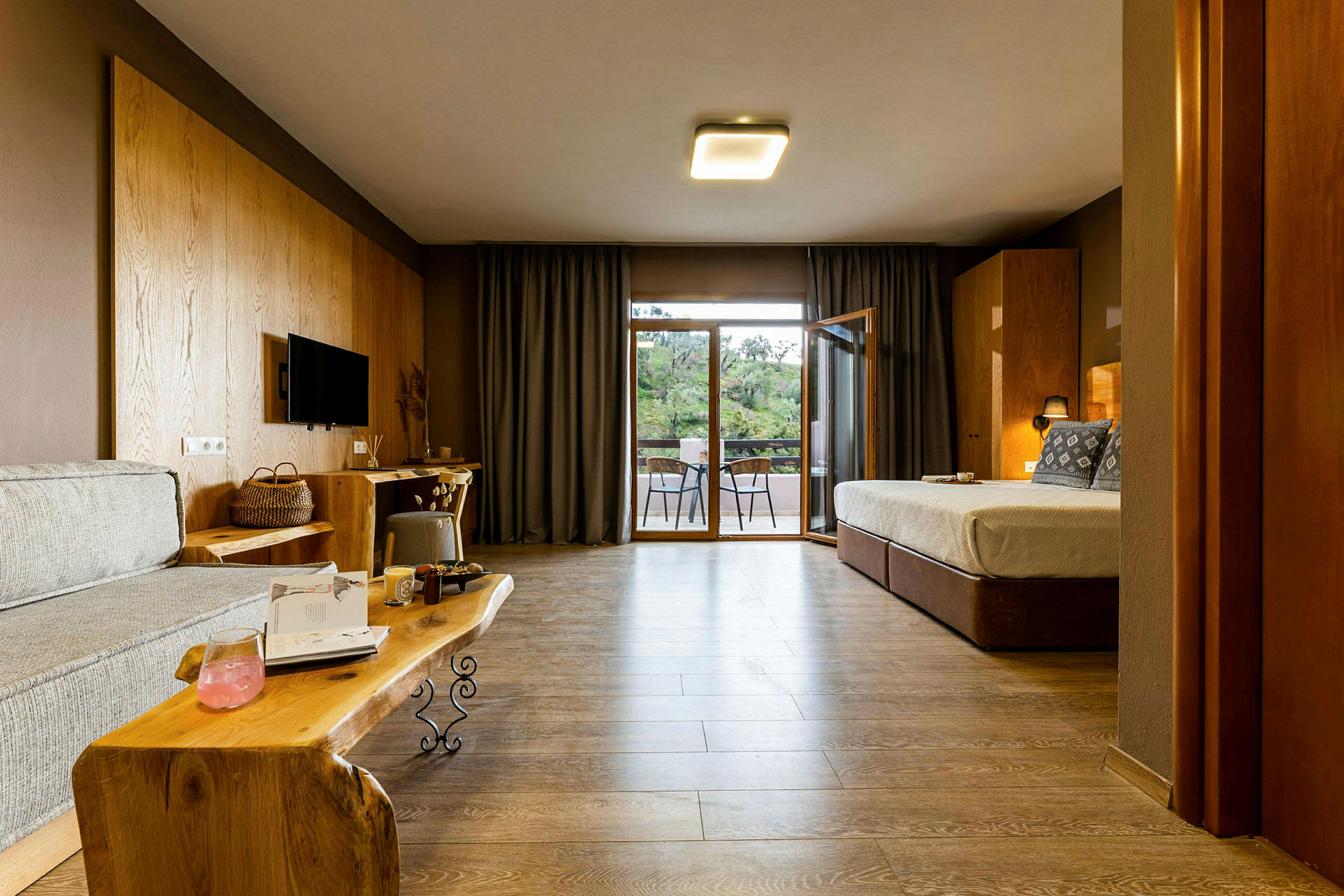 Ett hotellrum med soffa, säng, och en balkong utanför, inrett med trädetaljer. (AI-genererad text)
