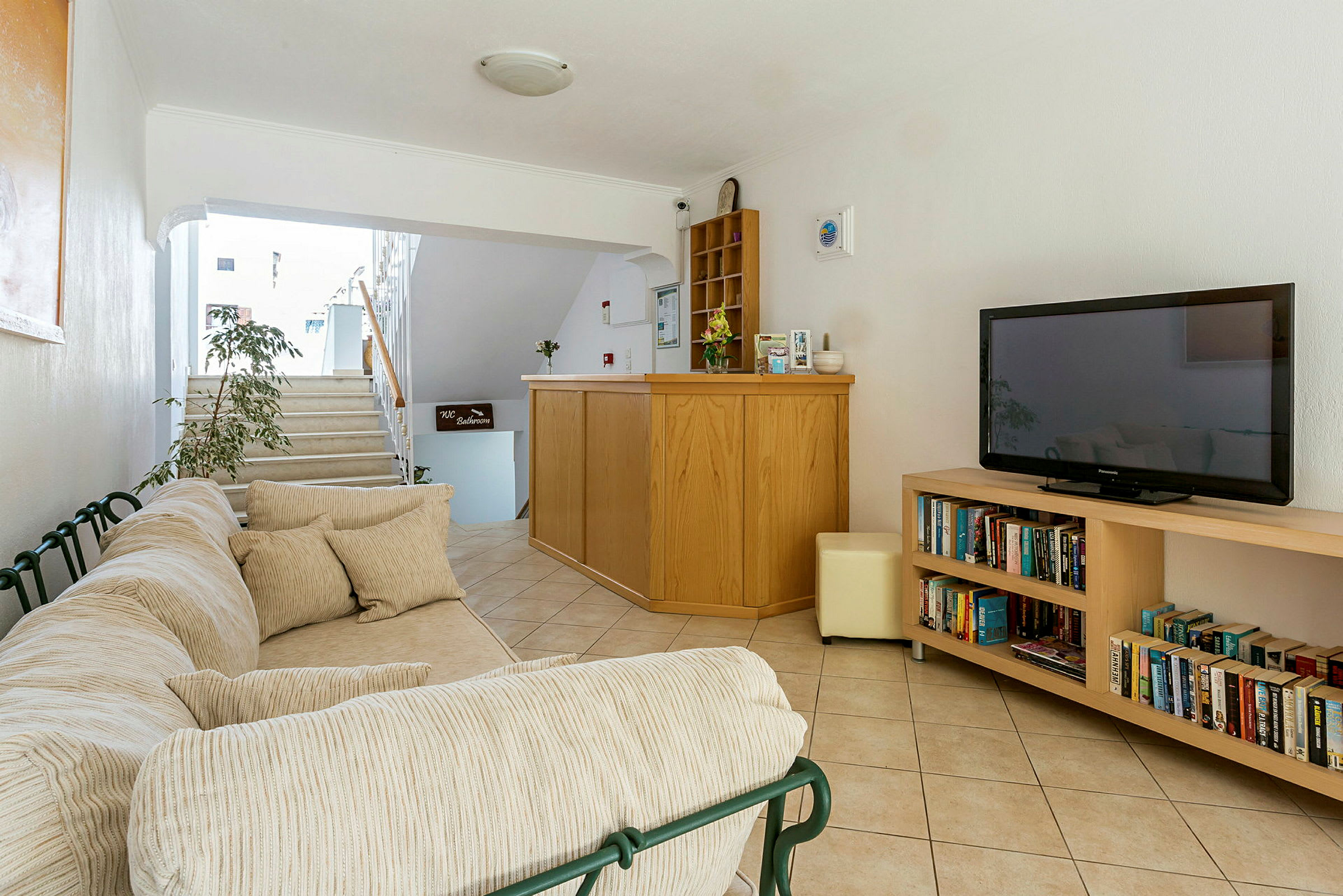 Soffa med kuddar, reception med disk och hylla samt bokhylla med böcker och TV. (AI-genererad text)