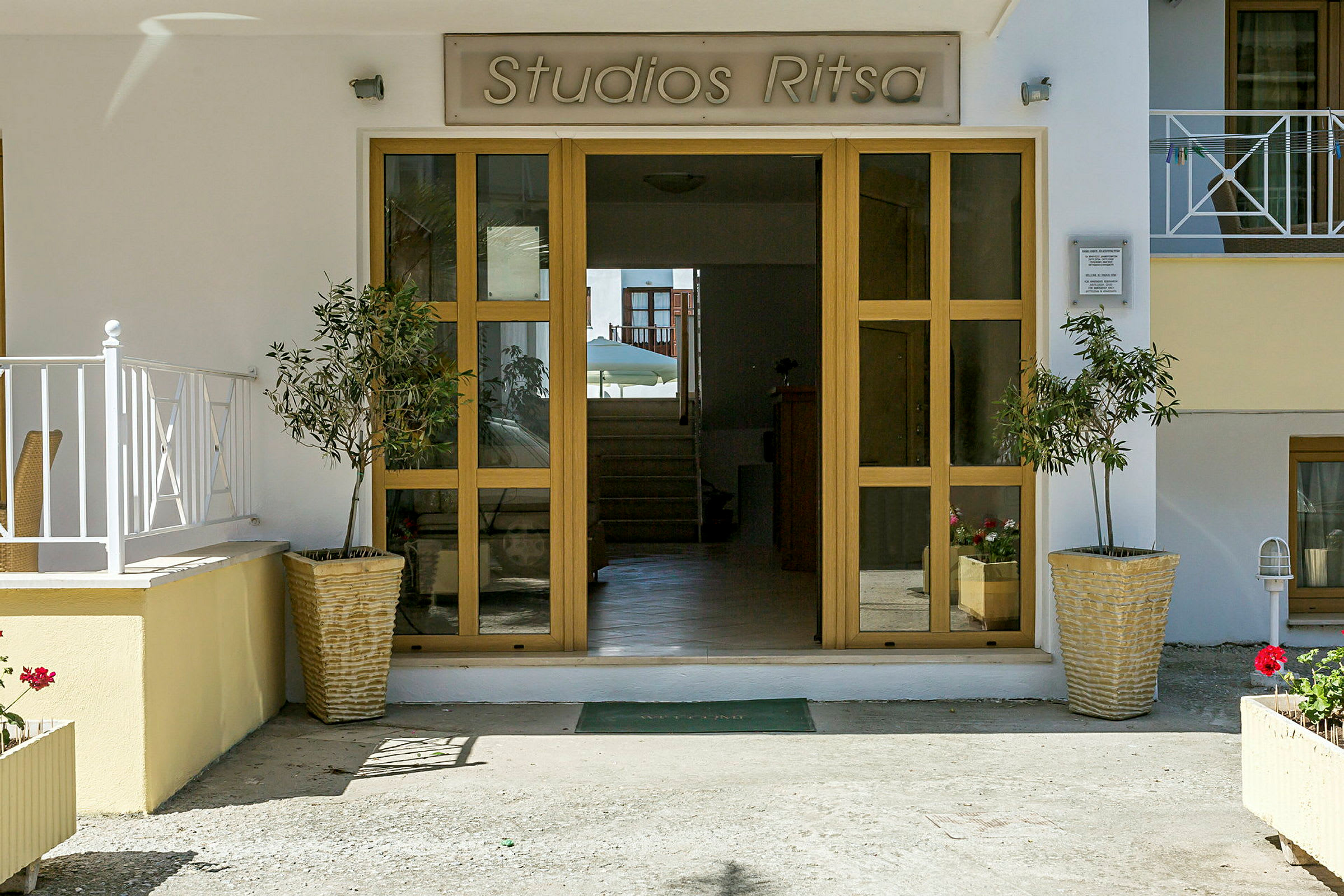 Entré till Studios Ritsa med glasdörrar och blomkrukor. (AI-genererad text)