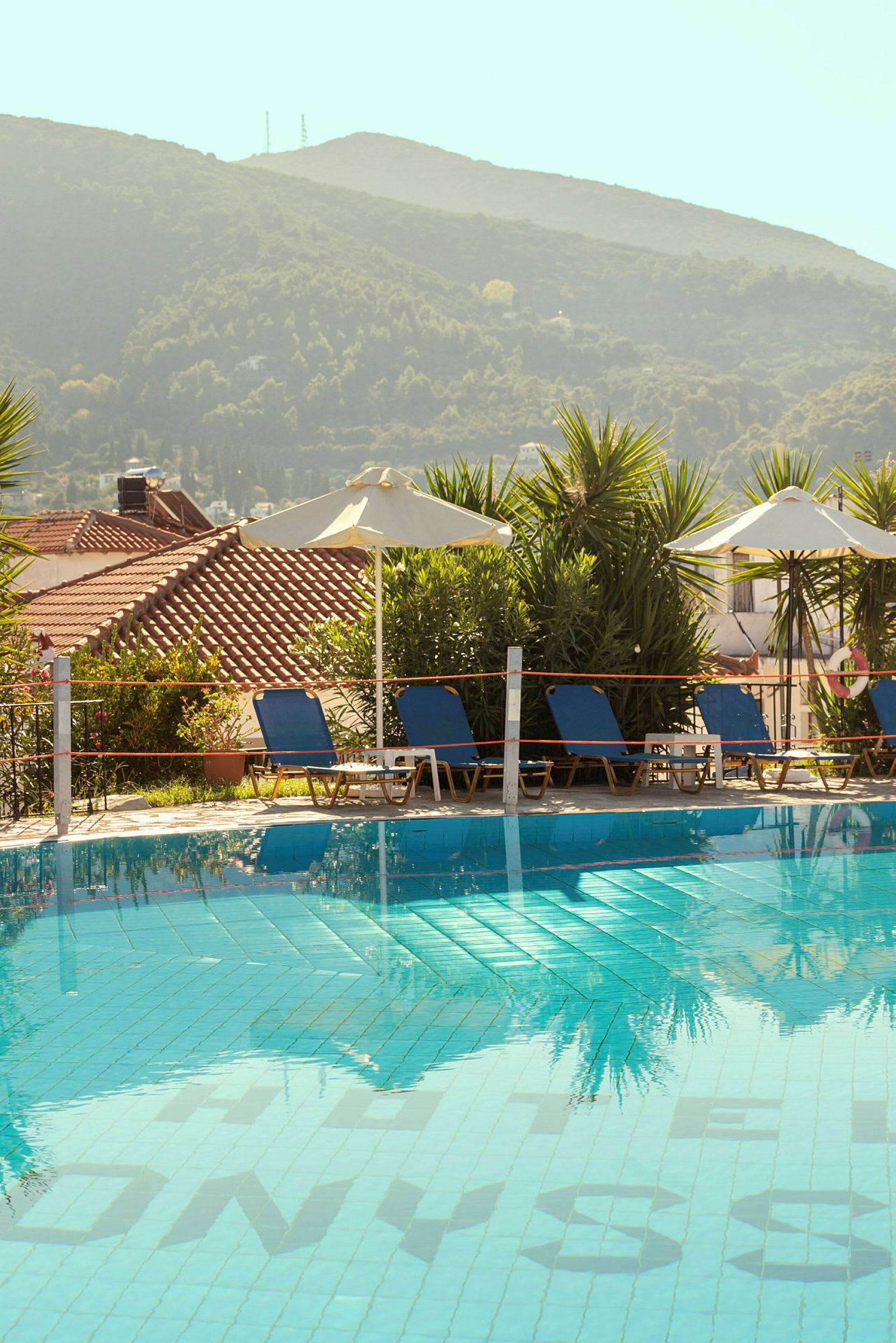 Pool med solstolar och parasoller med utsikt över gröna berg. (AI-genererad text)