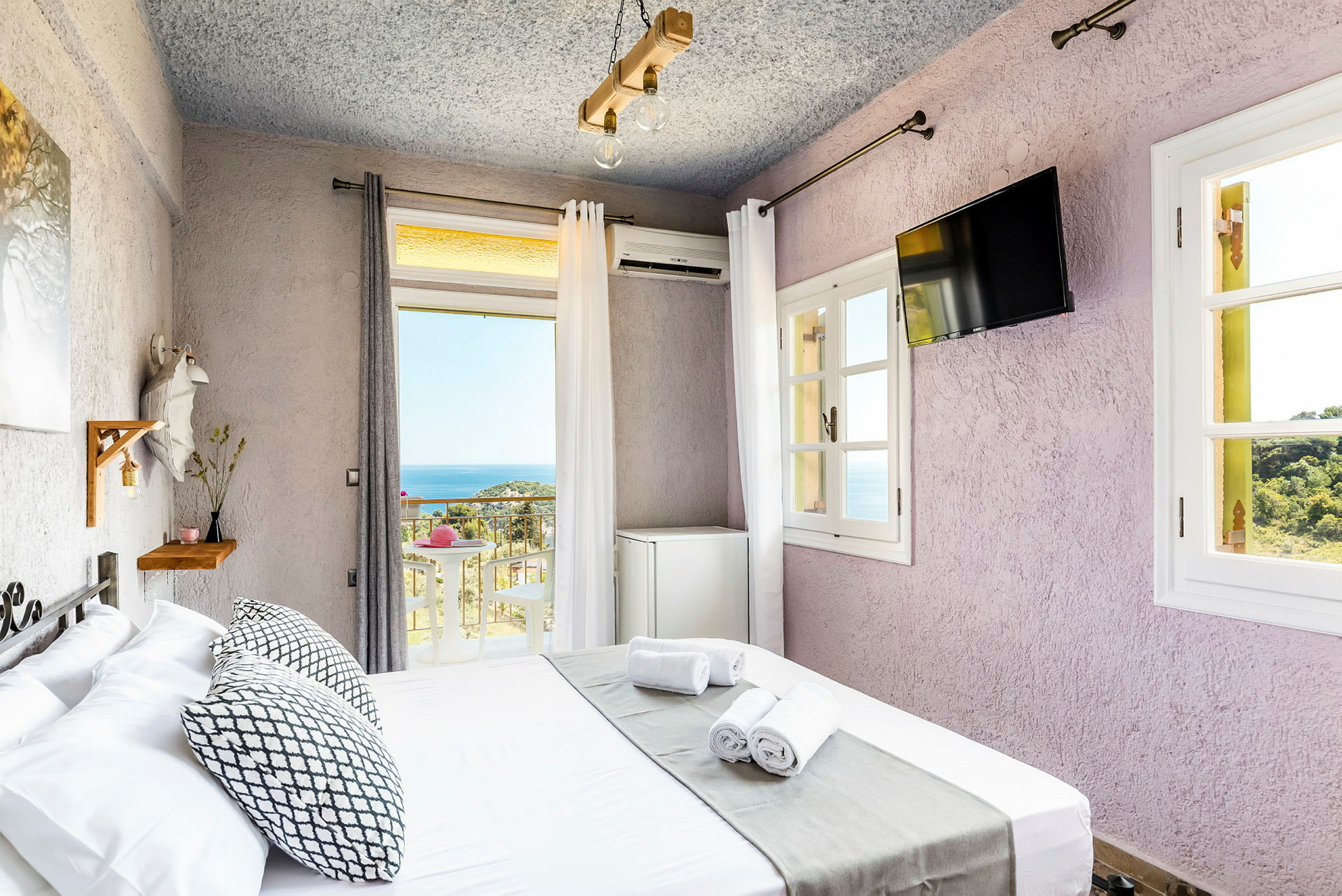 Ett rum med en säng, fönster med utsikt mot havet, och en liten inredningsdetalj med hylla och vägg-TV. (AI-genererad text)