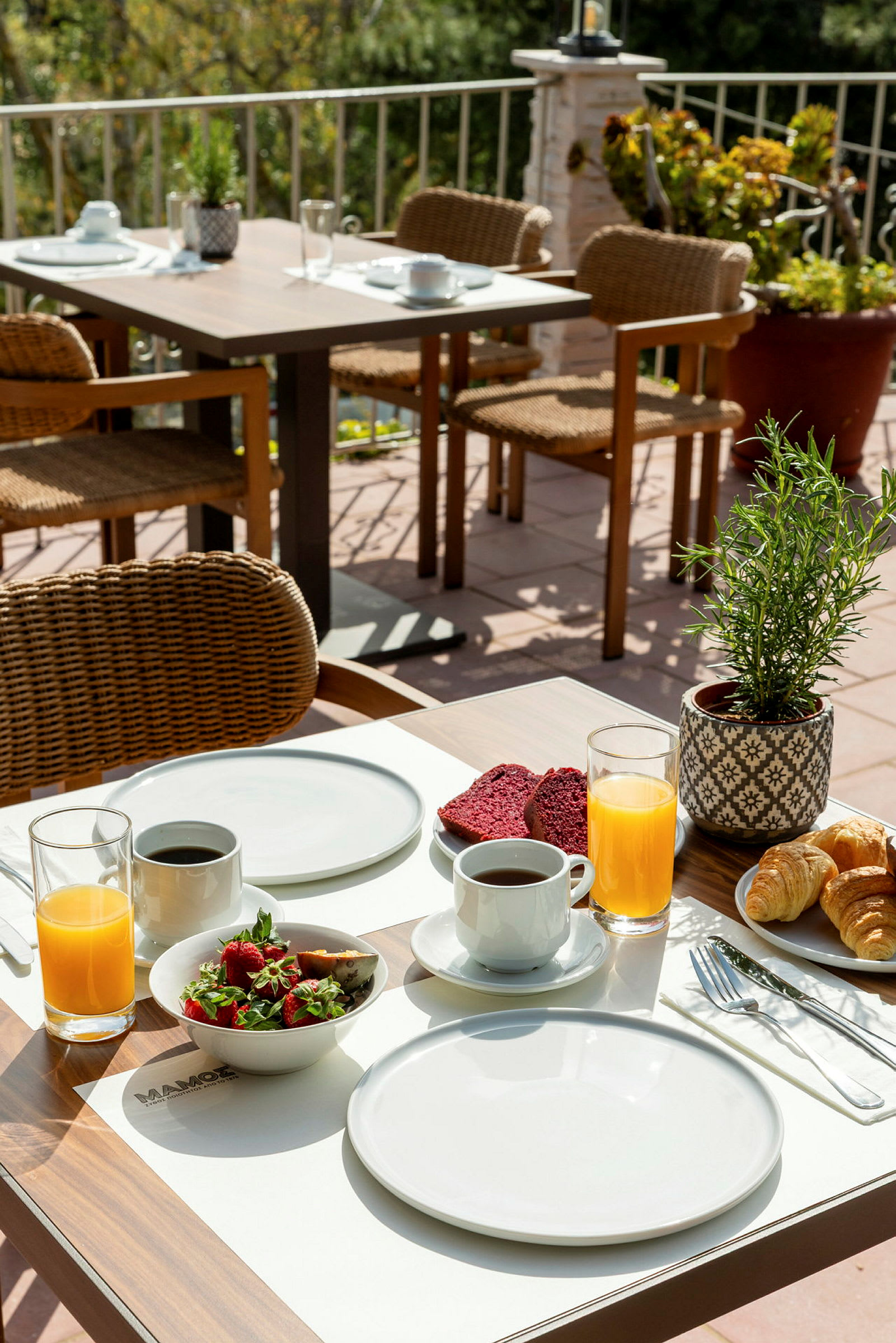Ett dukat bord med frukostbestick, kaffe, juice och frukostmat på en terrass. (AI-genererad text)
