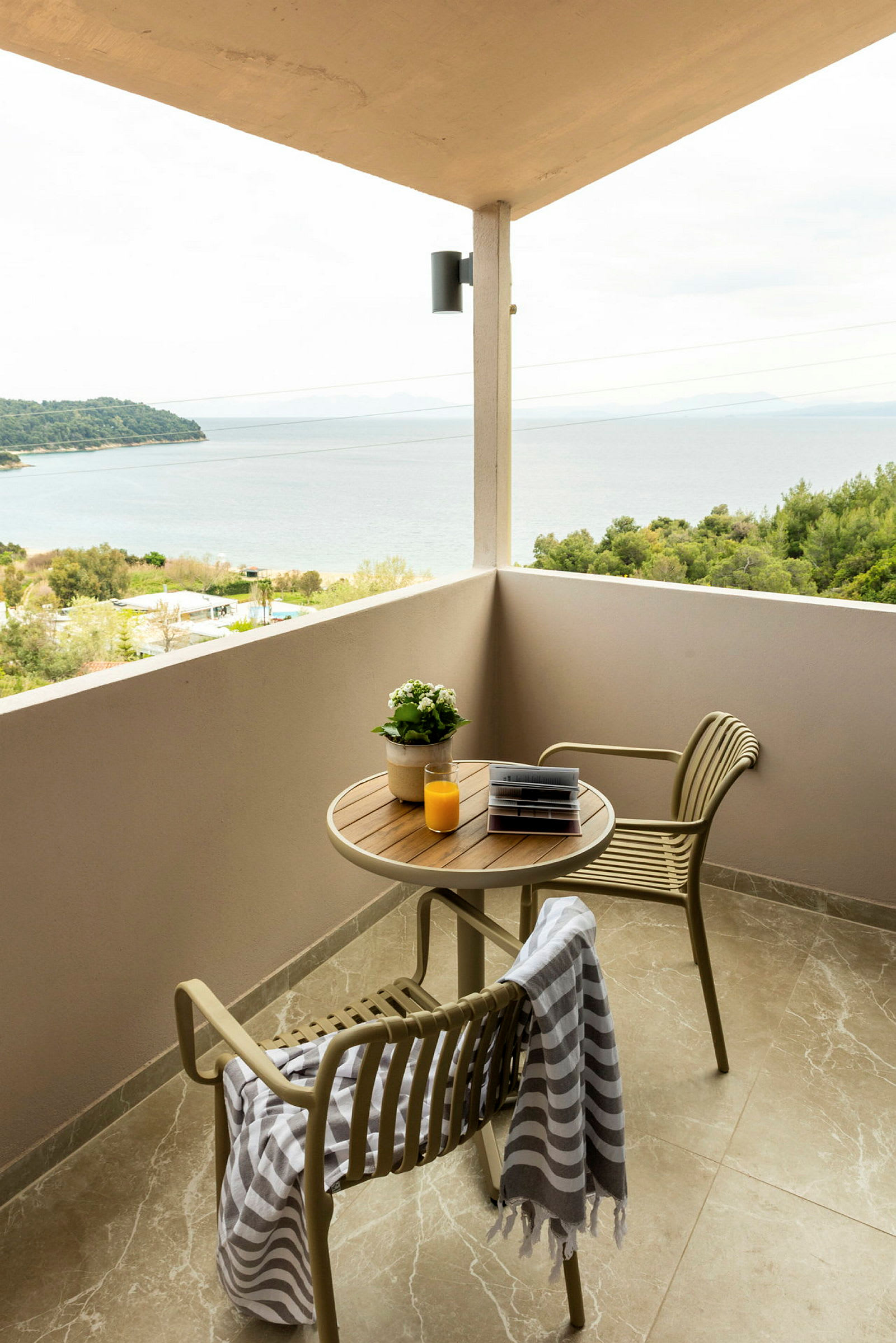 En balkong med utsikt över havet, två stolar och ett bord med en växt, en bok och ett glas apelsinjuice. (AI-genererad text)