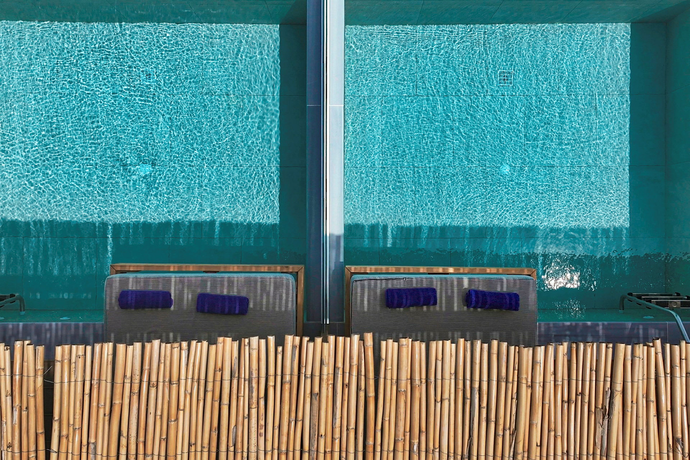 Två solstolar vid en pool med bambu som avskiljare. (AI-genererad text)
