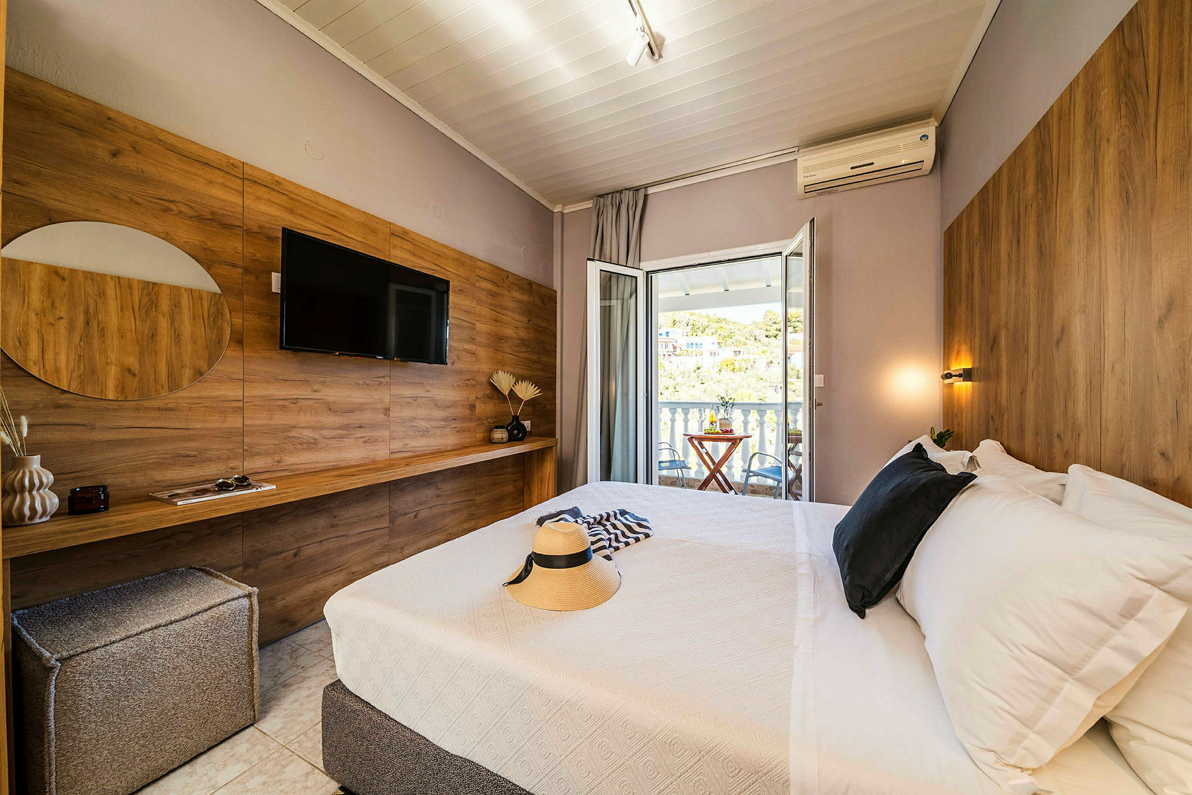 Ett hotellrum med en säng, en TV på väggen och en balkong med utsikt. (AI-genererad text)