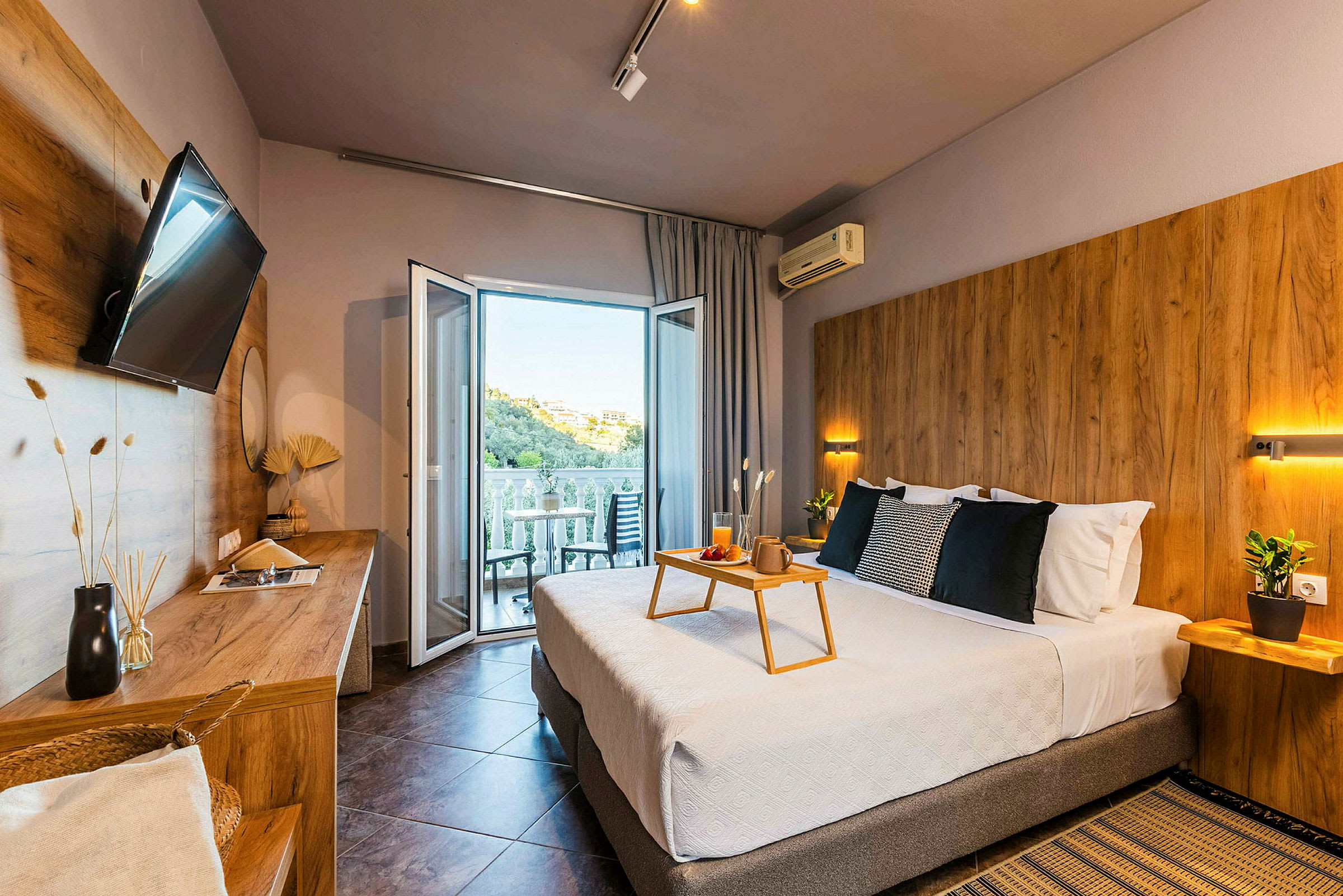 Modernt hotellrum med dubbelsäng, sittmöbler på balkongen och utsikt över en grönskande kulle. (AI-genererad text)