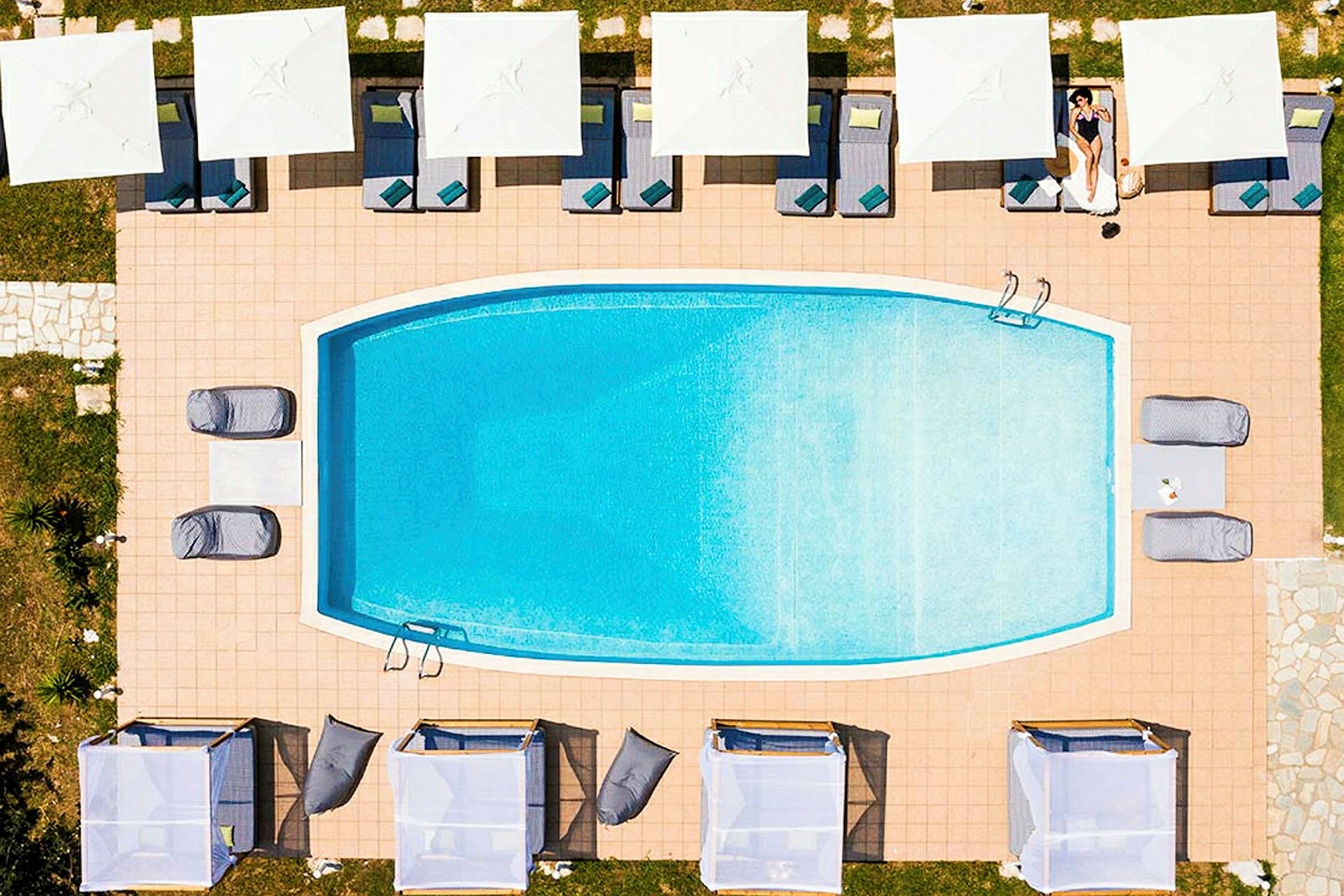 En rektangulär pool omgiven av solstolar med parasoller ovanifrån. (AI-genererad text)