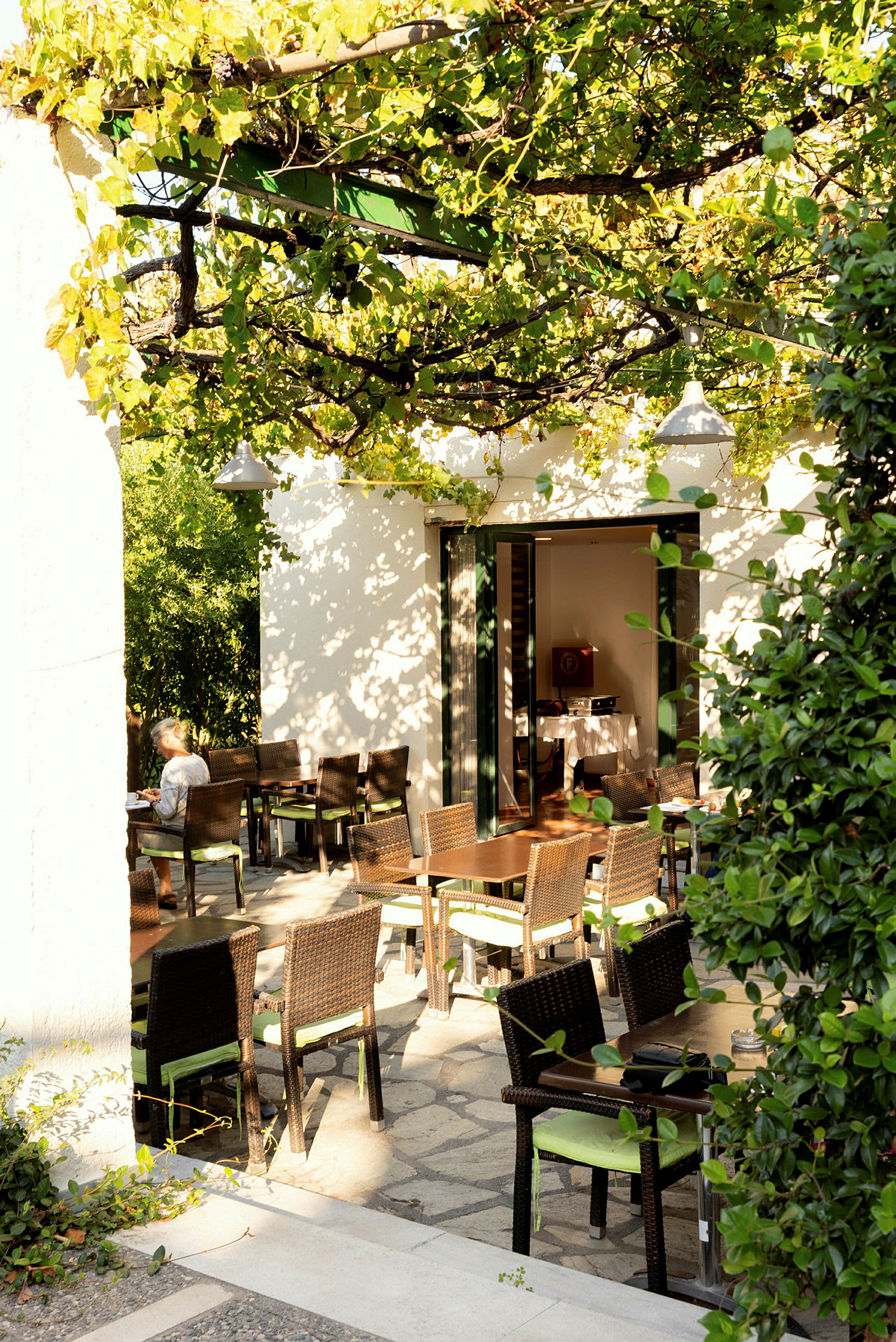 Ett café med bord och stolar på en stenterrass, omgiven av grönska. (AI-genererad text)