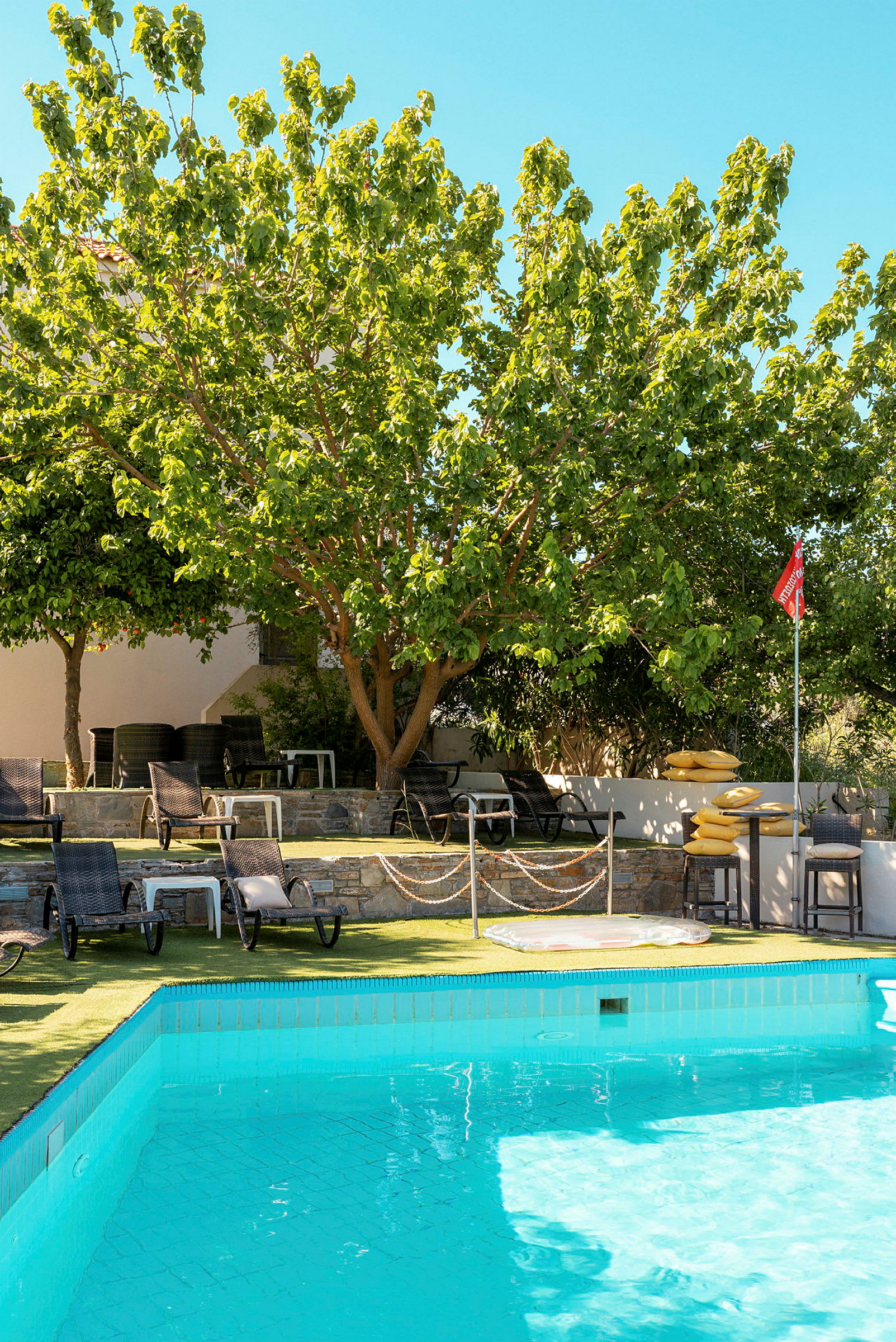 En pool med solstolar och gröna träd i bakgrunden. (AI-genererad text)