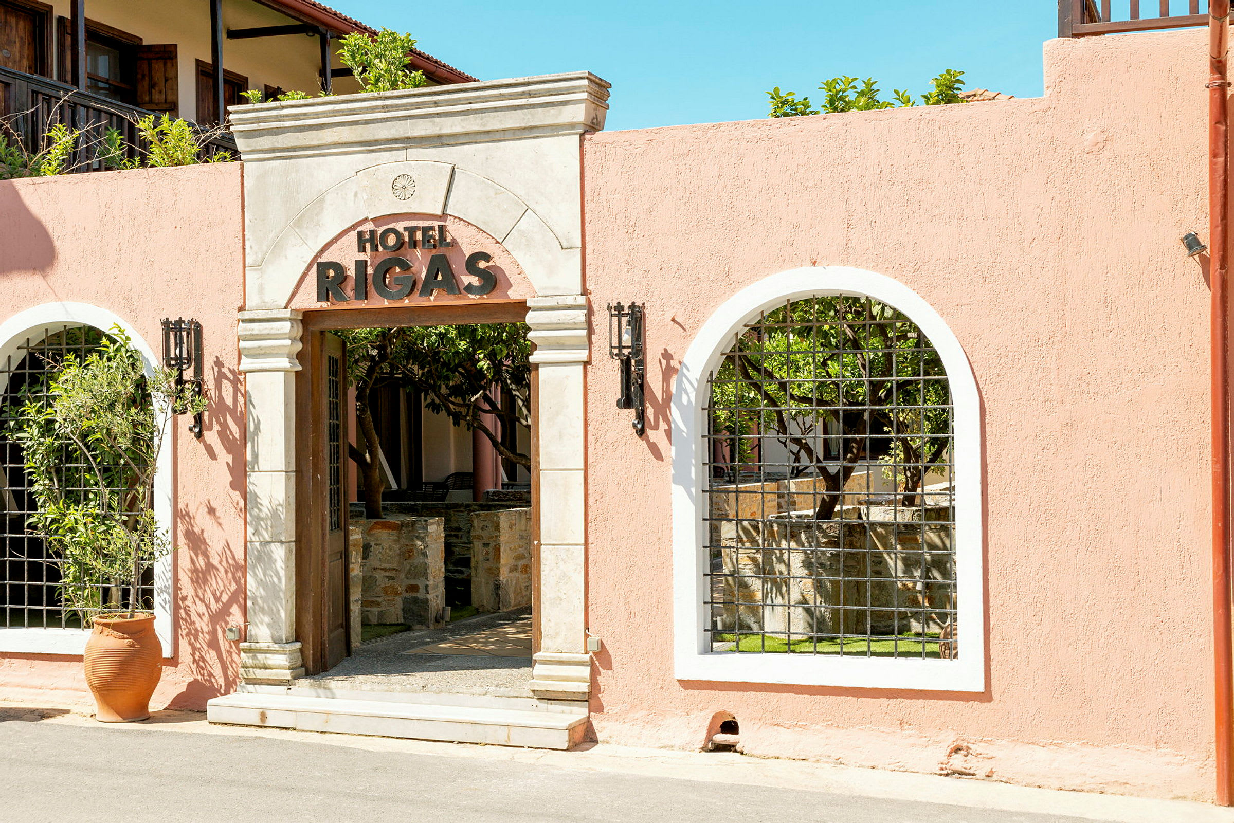 Entrén till Hotel Rigas, med en ljusrosa vägg och dekorativ båge. (AI-genererad text)