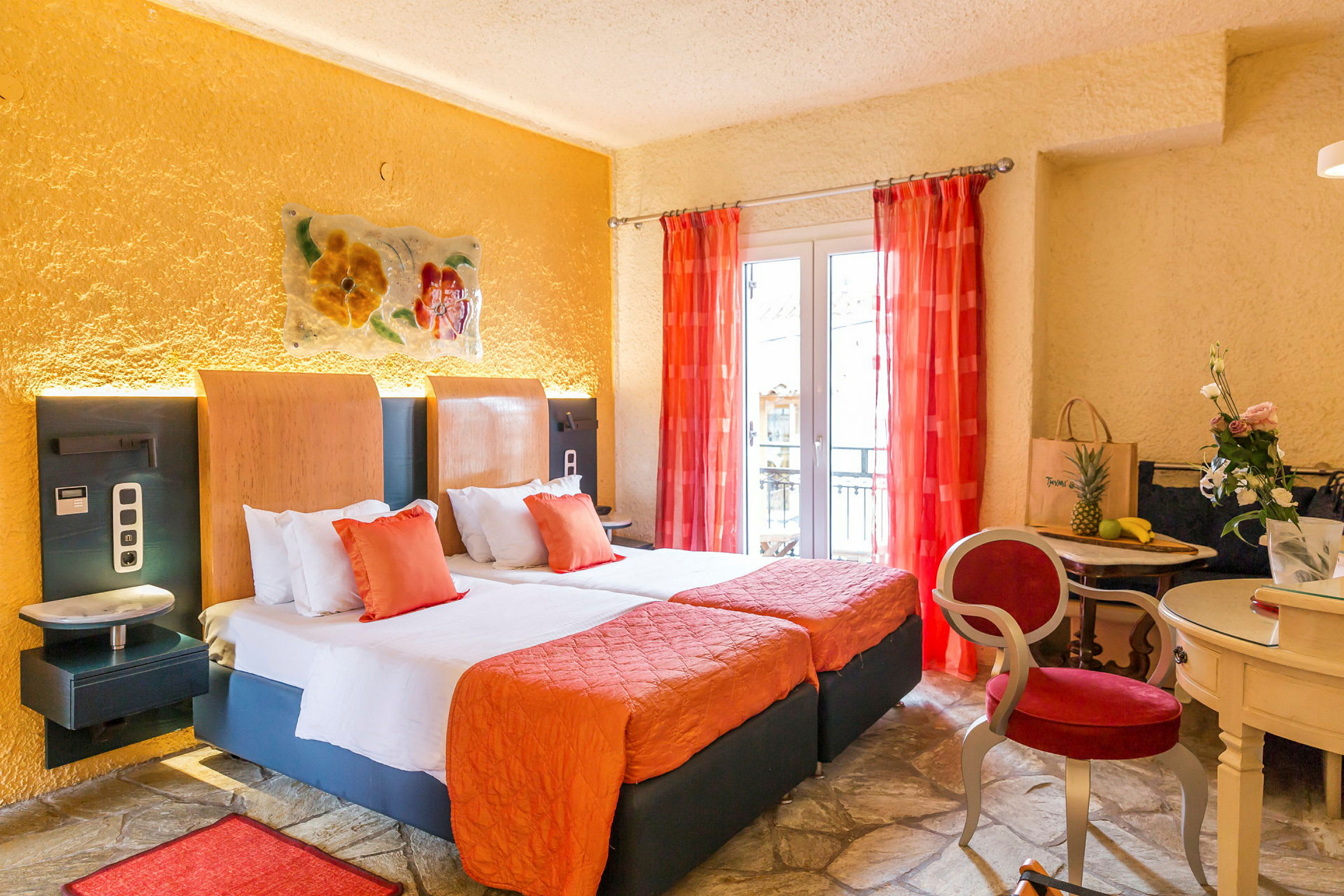 Ett hotellrum med två sängar, orange inredning och röda gardiner, samt ett mindre bord med stolar och dekorationer. (AI-genererad text)
