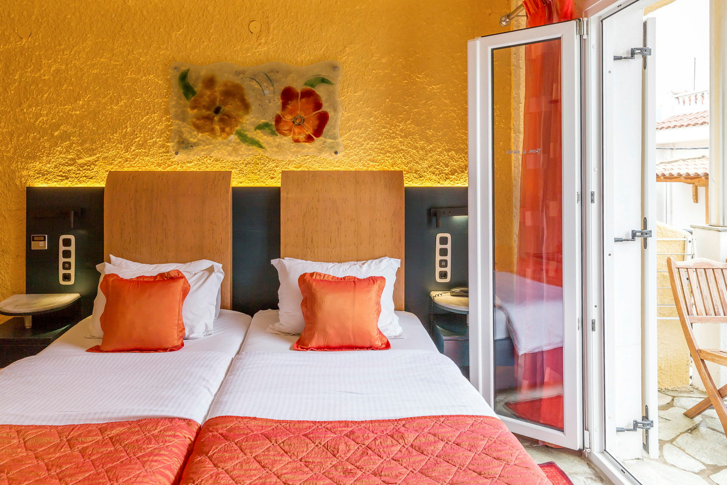 Hotellrum med två enkelsängar, oranga dekorationskuddar och en balkong. (AI-genererad text)