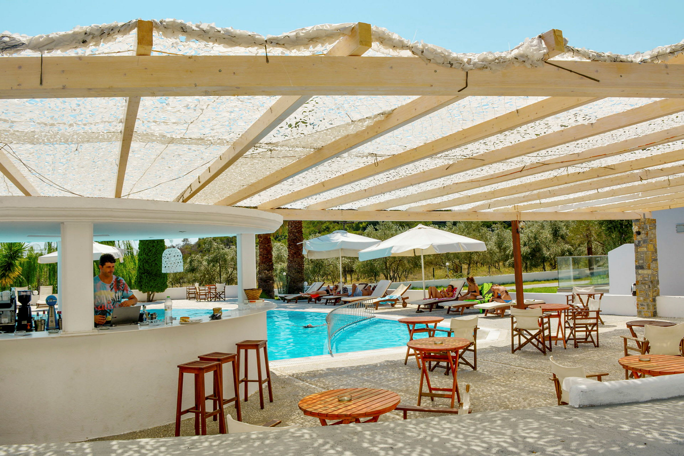 En bar med sittplatser bredvid en pool omgiven av solstolar och parasoller. (AI-genererad text)