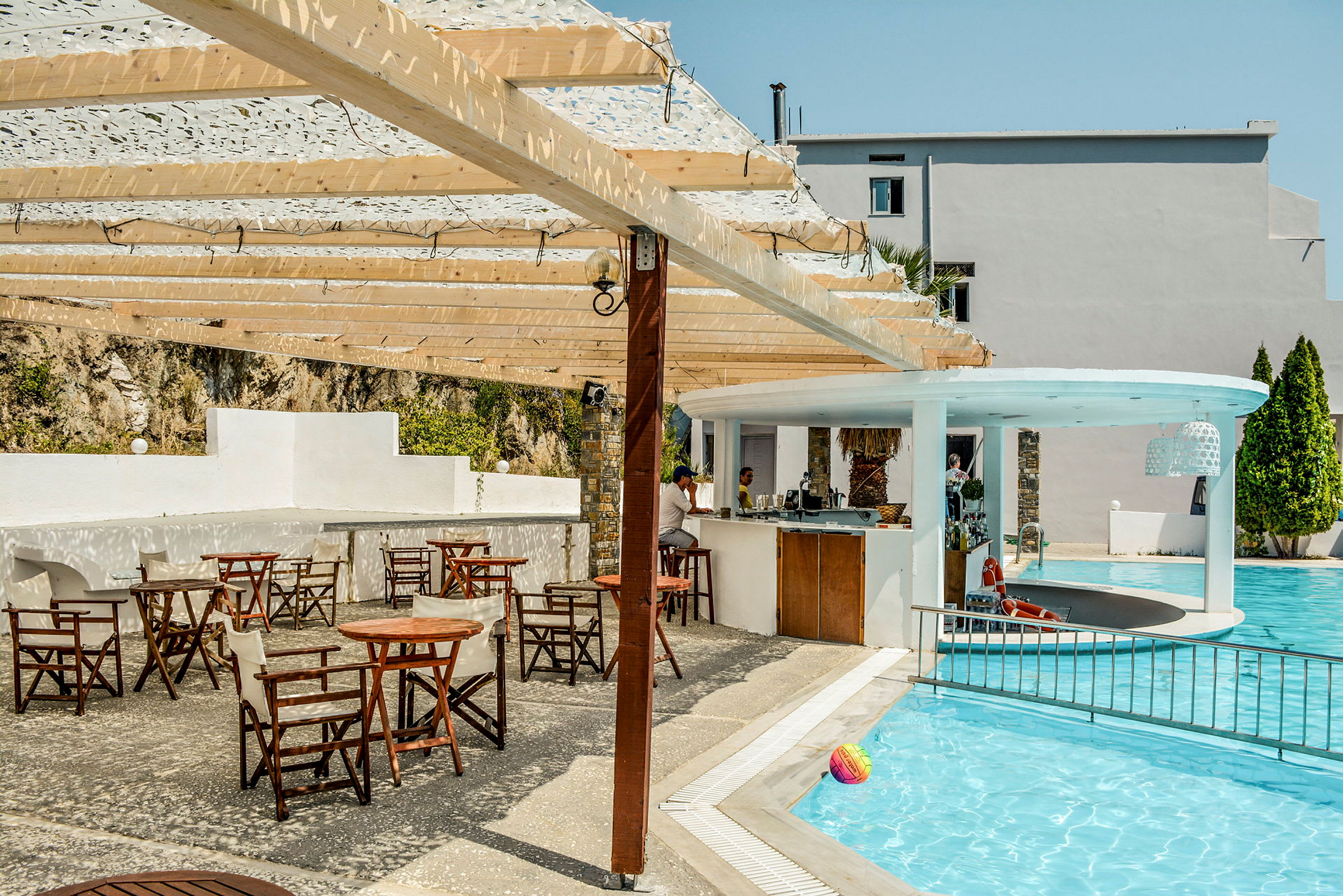 Utomhuspoolområde med en bar och flera bord och stolar under en träpergola. (AI-genererad text)