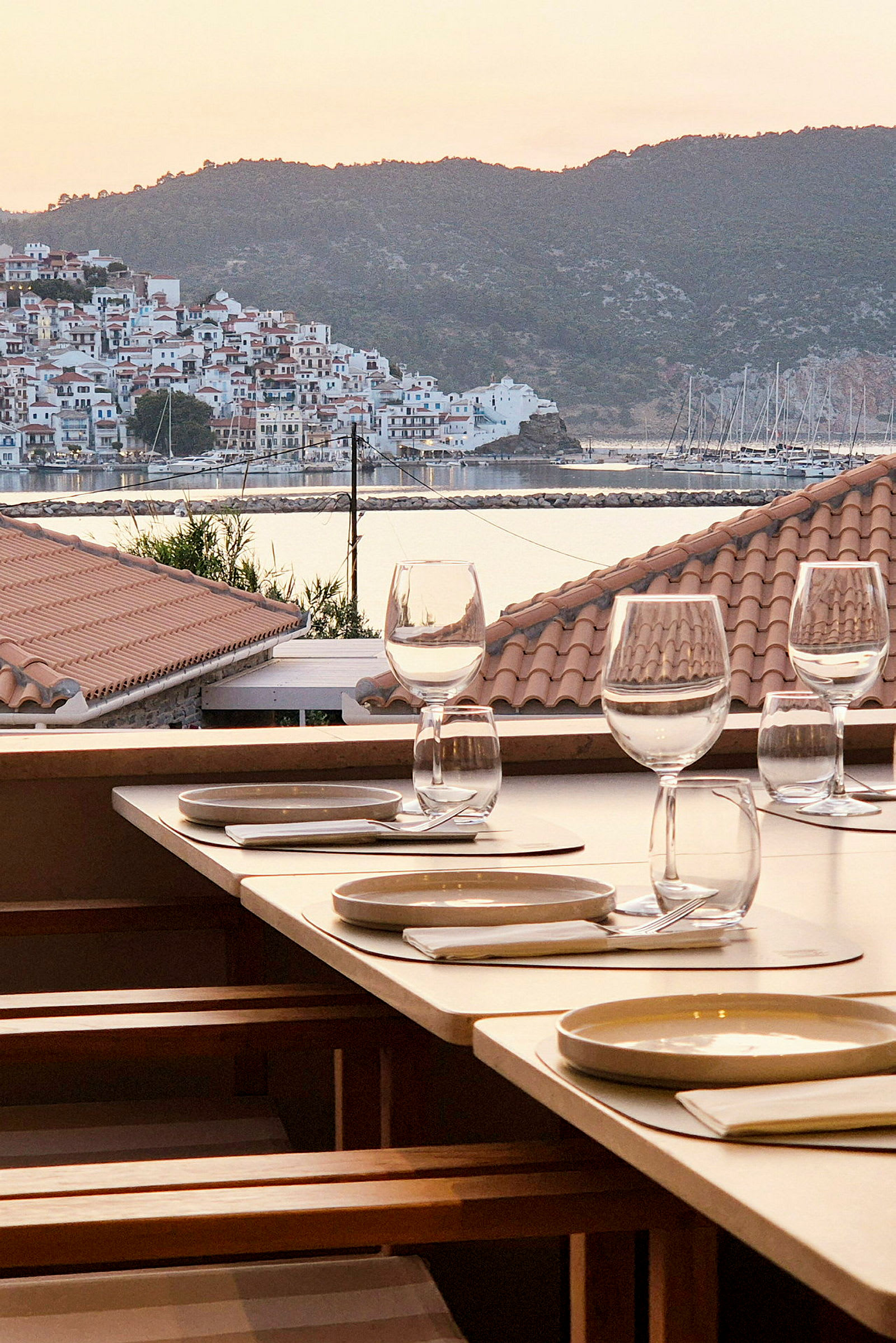 En utomhusrestaurang med dukade bord, i bakgrunden syns en kuststad och en marina. (AI-genererad text)