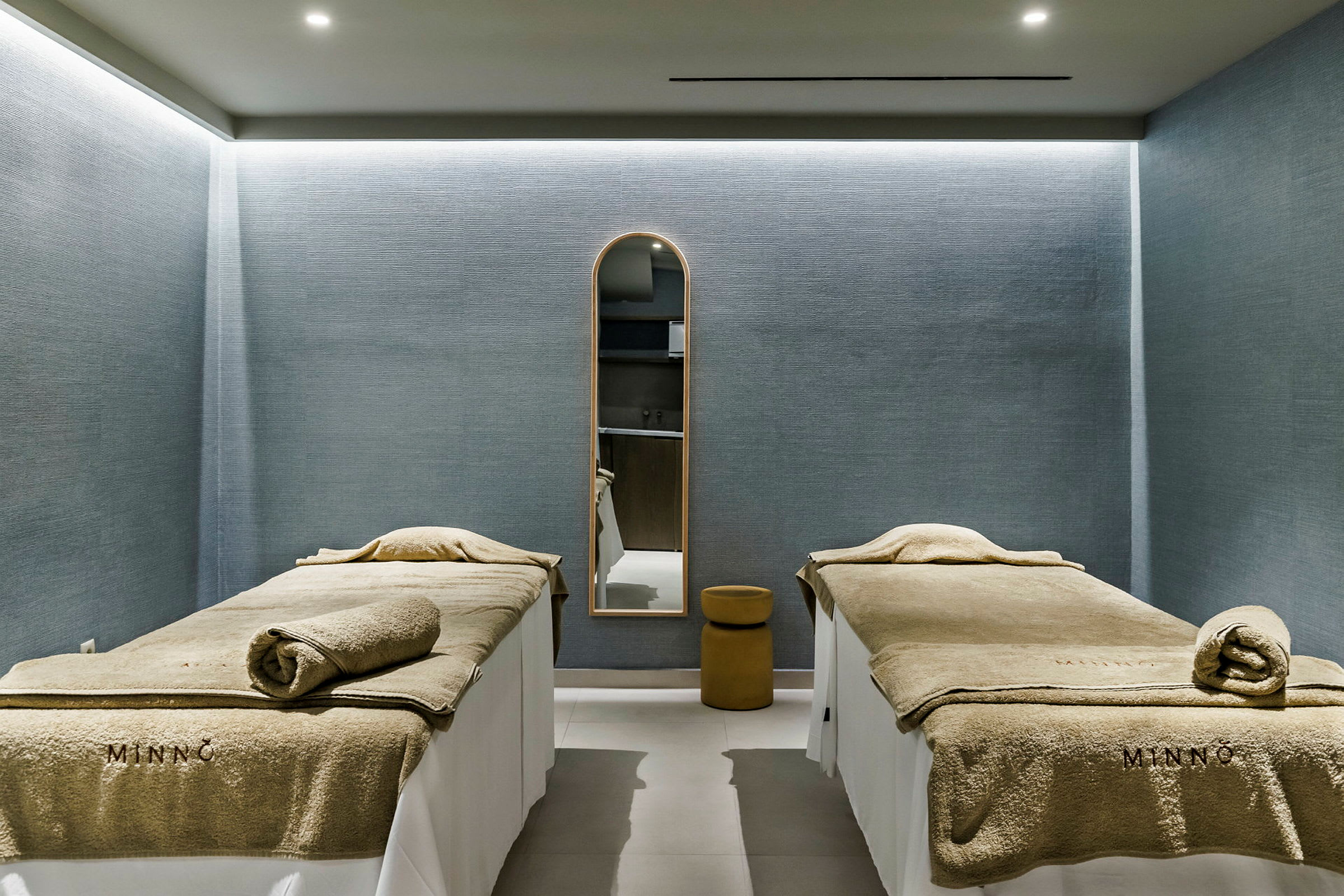 Två massagebänkar i ett rum med blå väggar och ett spegel på väggen. (AI-genererad text)
