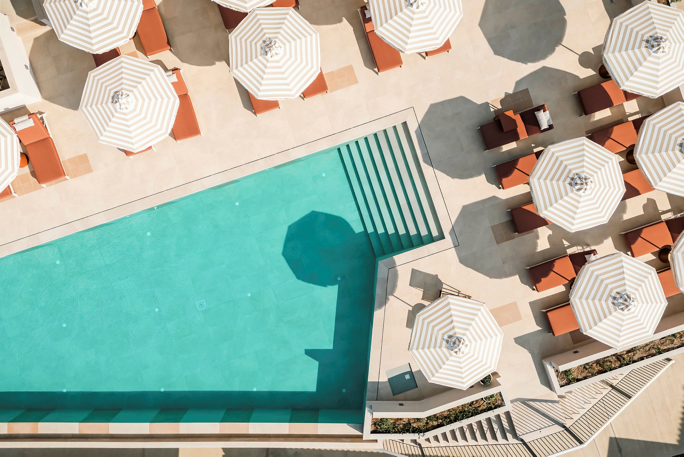 En pool med turkost vatten och omgivande solstolar under randiga parasoller. (AI-genererad text)