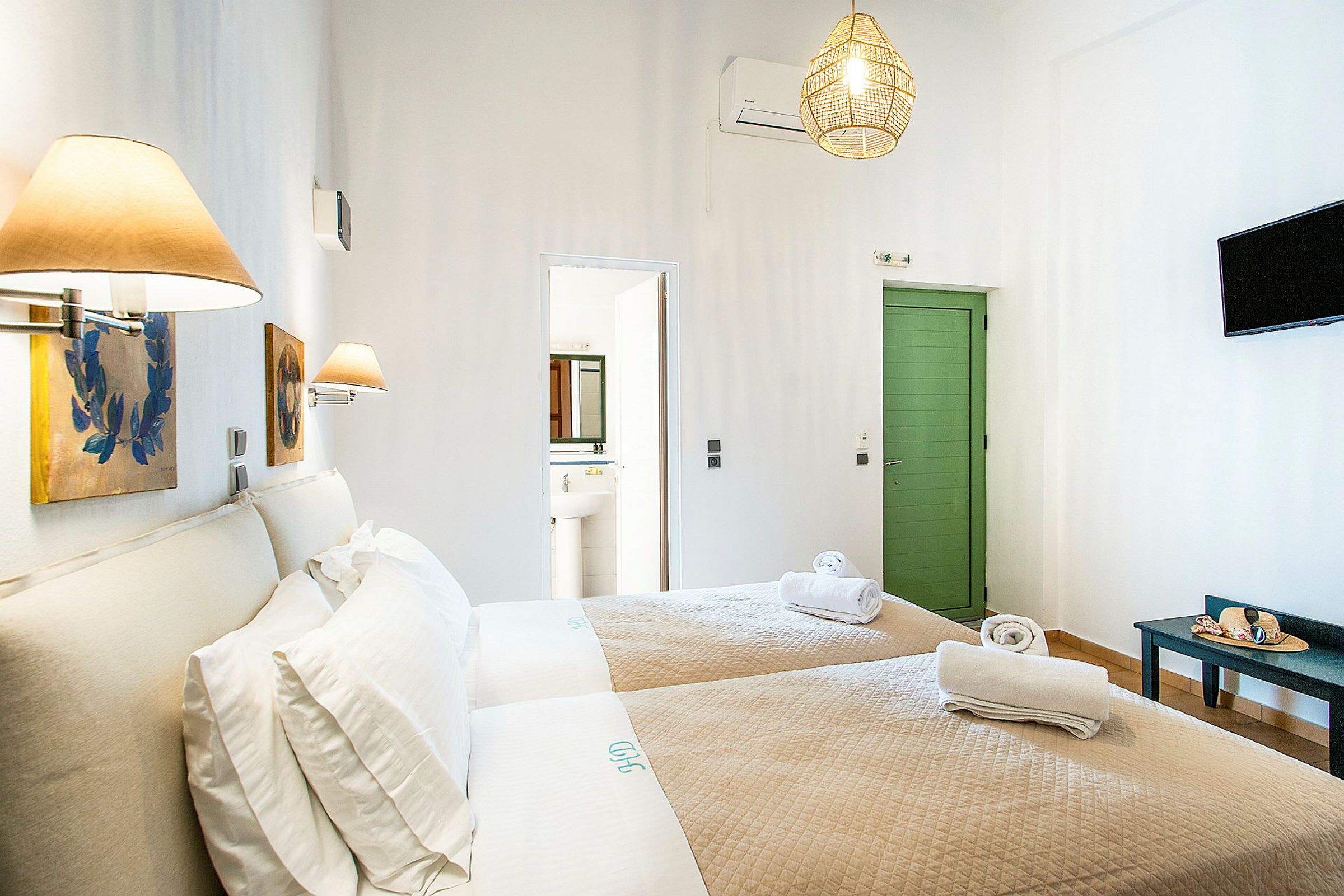 Hotellrum med två enkelsängar och beige sängkläder, dekorerat med vägglampor och tavlor. En dörr leder till badrummet. (AI-genererad text)