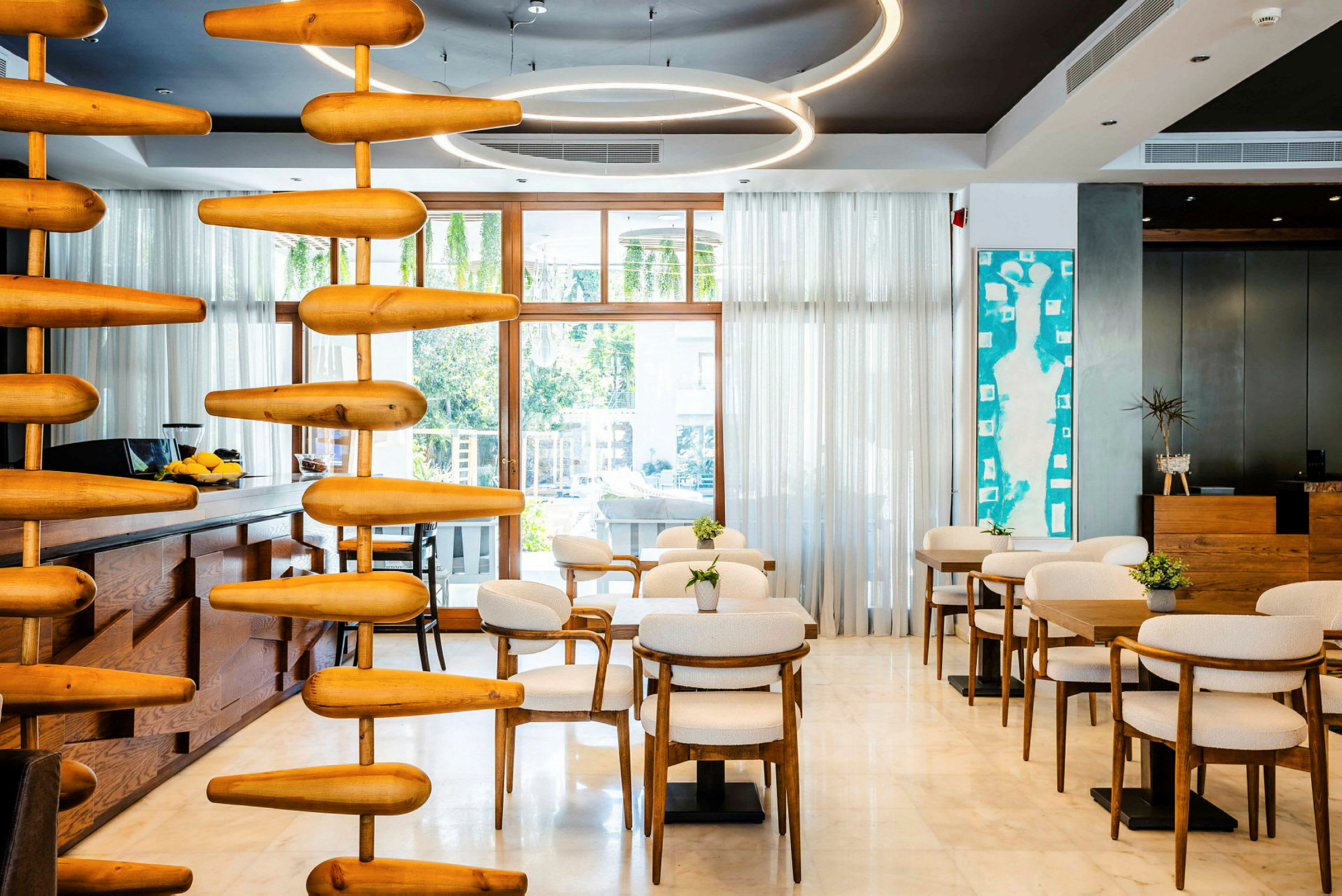 Ett modernt och ljust inrett café eller loungemiljö med trä och vita stolar, stora fönster och väggdekorationer. (AI-genererad text)