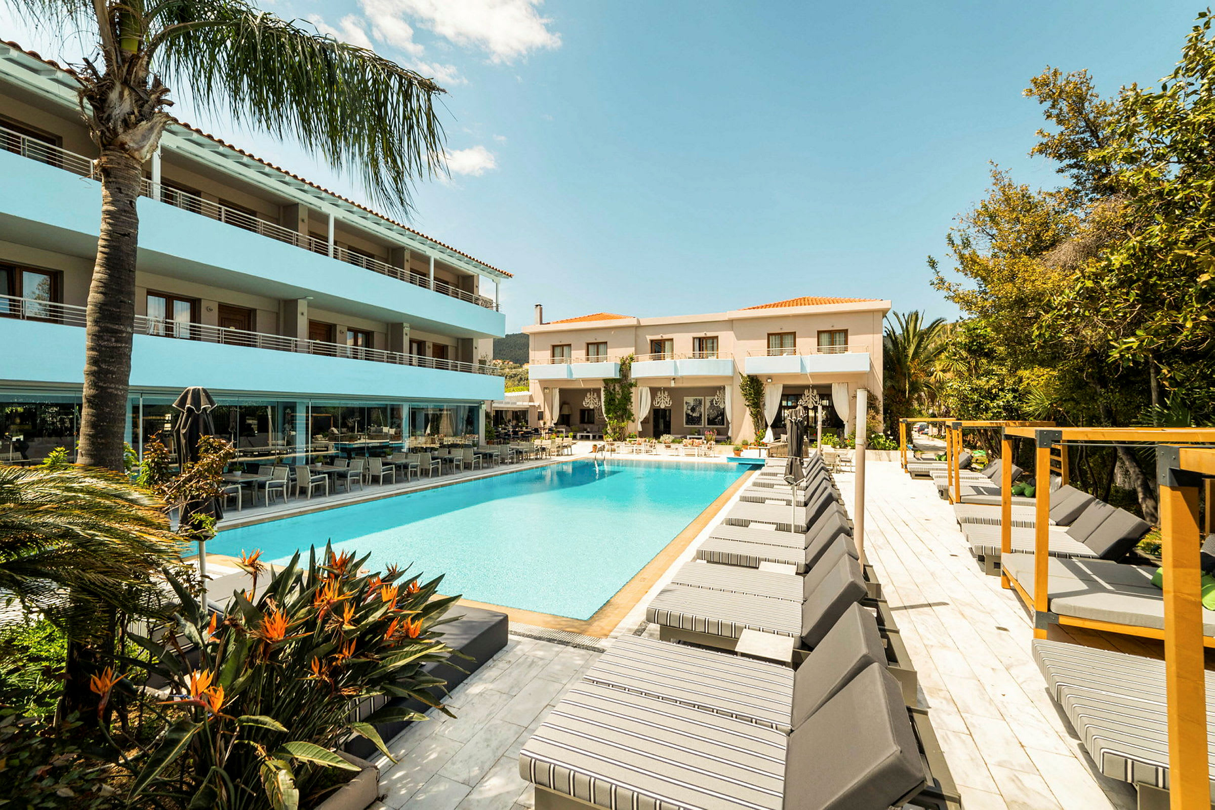En hotellpool omgiven av solstolar och byggnader under en klarblå himmel. (AI-genererad text)