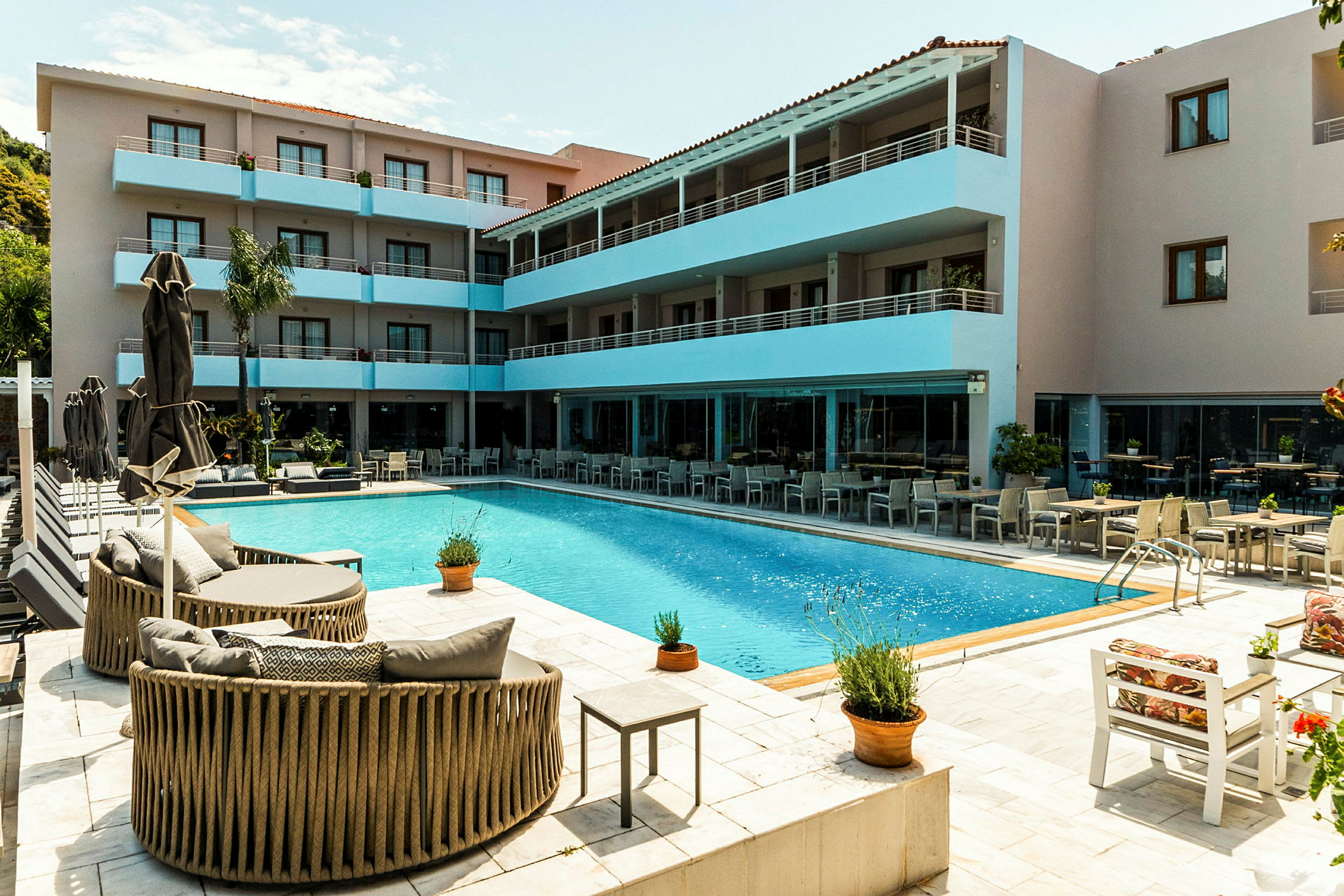 Bild av ett hotellområde med en pool, omgiven av sittmöbler och en byggnad i flera våningar med balkonger. (AI-genererad text)