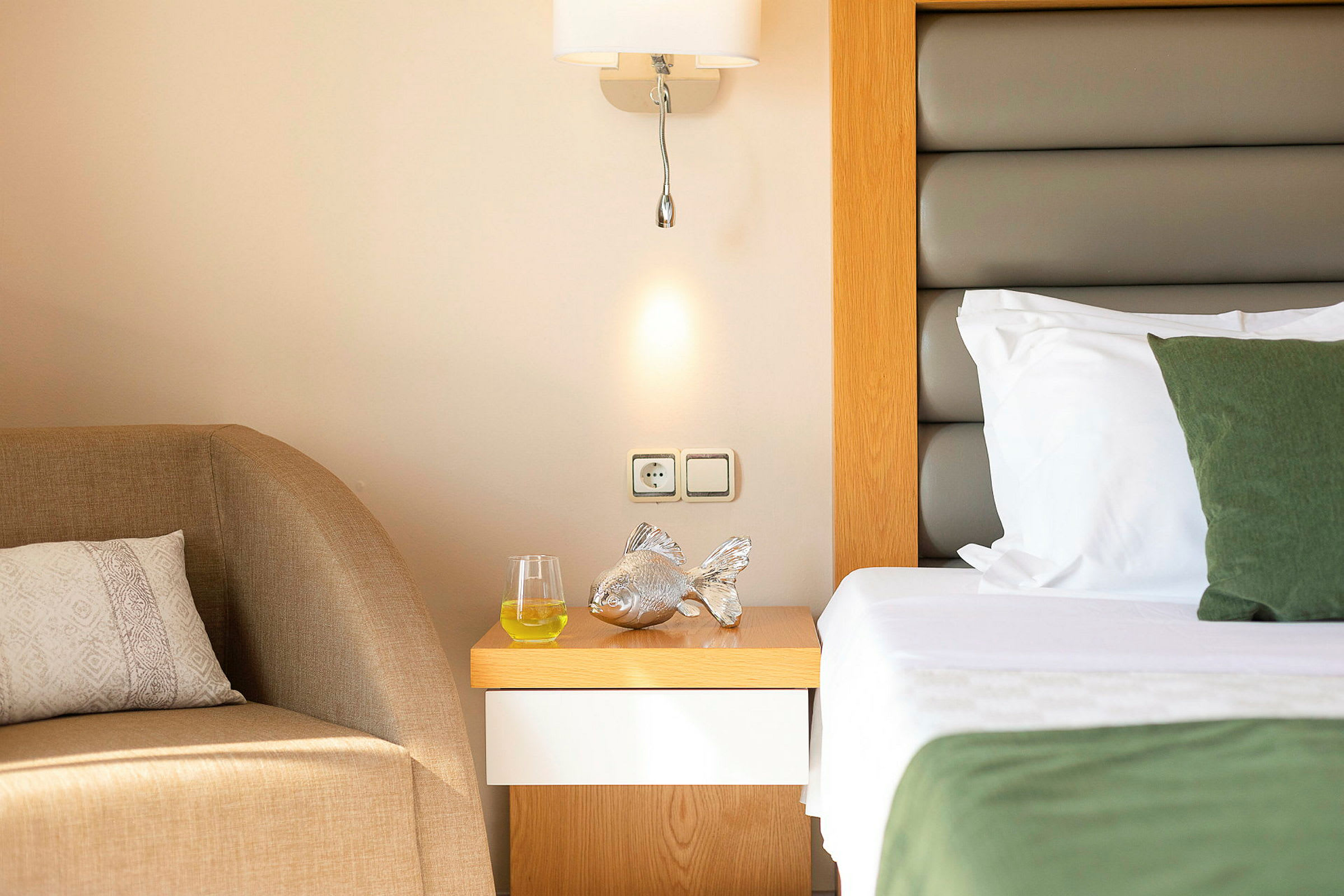 Ett hotellrum med en närbild på nattduksbord med en silverfärgad prydnad, ett glas med dryck och en säng bredvid. (AI-genererad text)