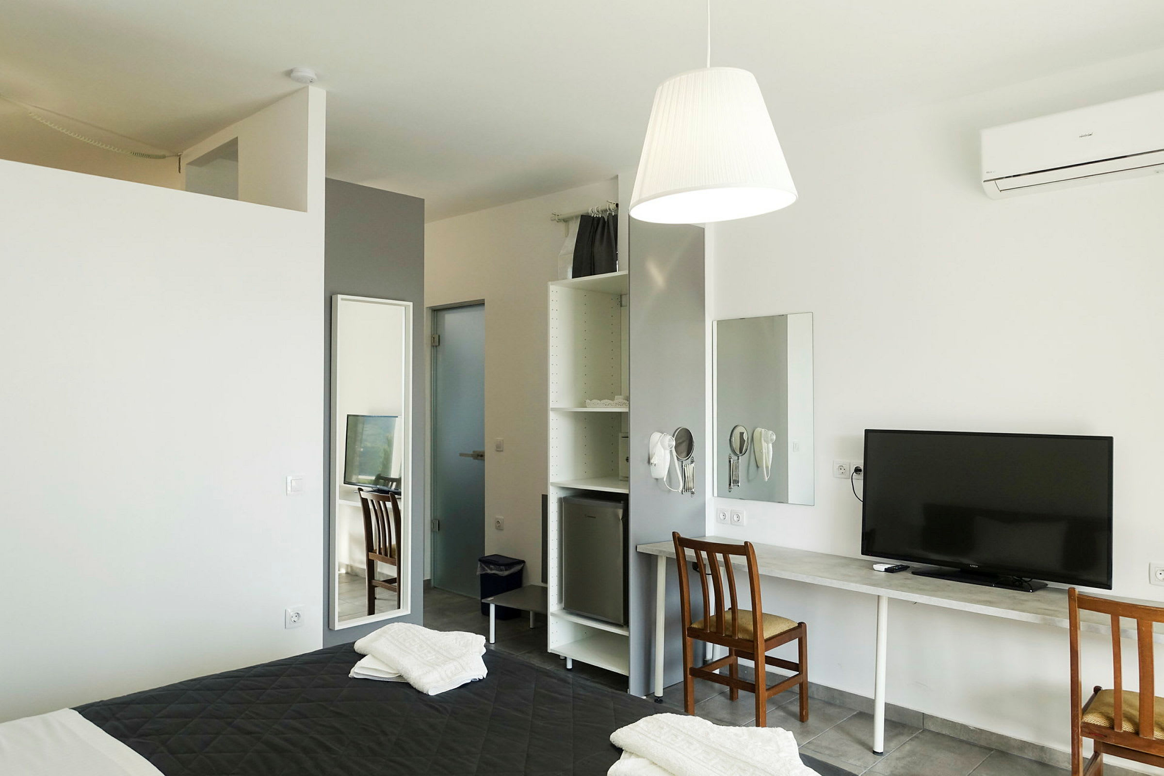 Ett hotellrum med en säng, spegel, skrivbord med stolar och en TV. (AI-genererad text)