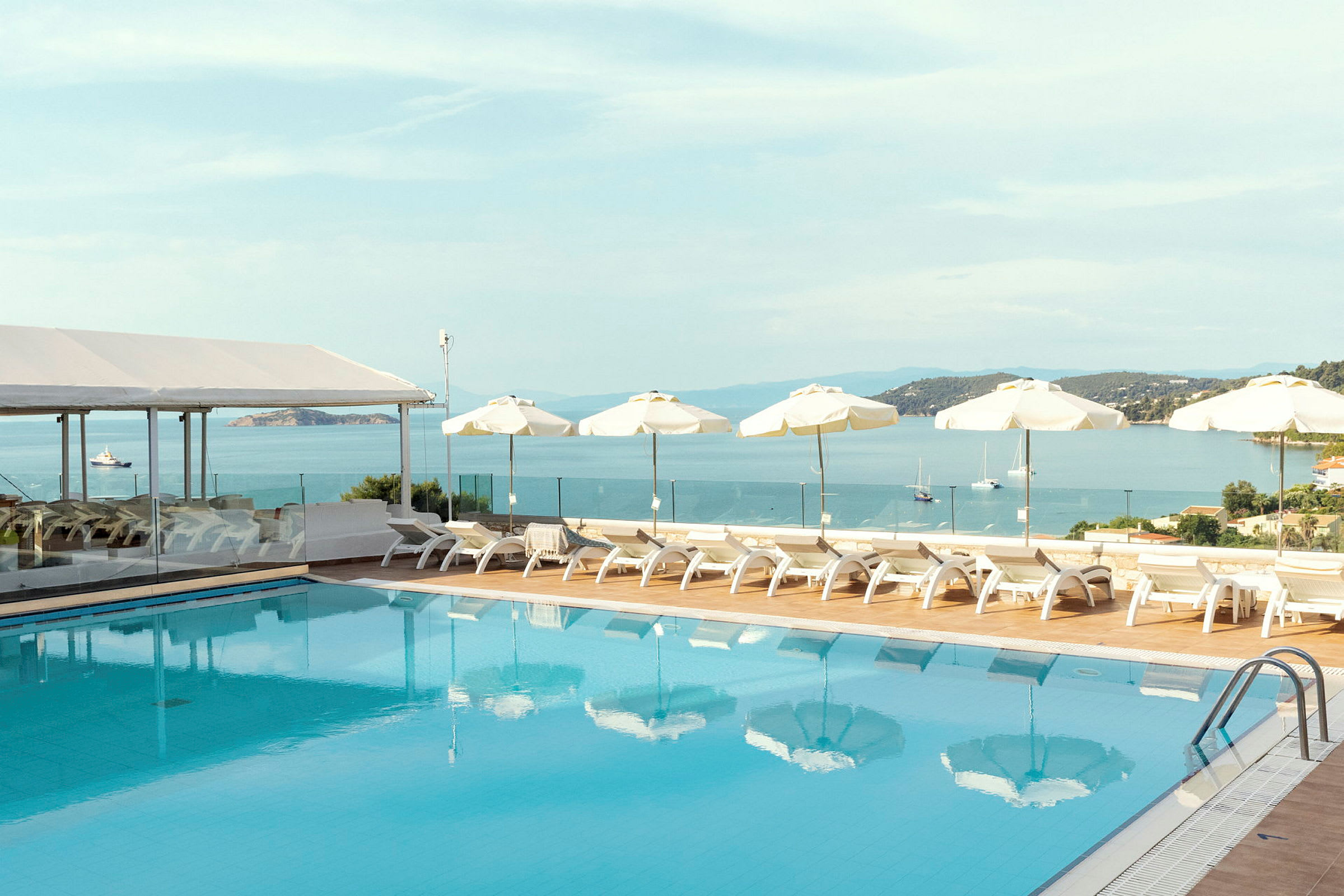 En pool med solstolar och parasoller vid havet. (AI-genererad text)