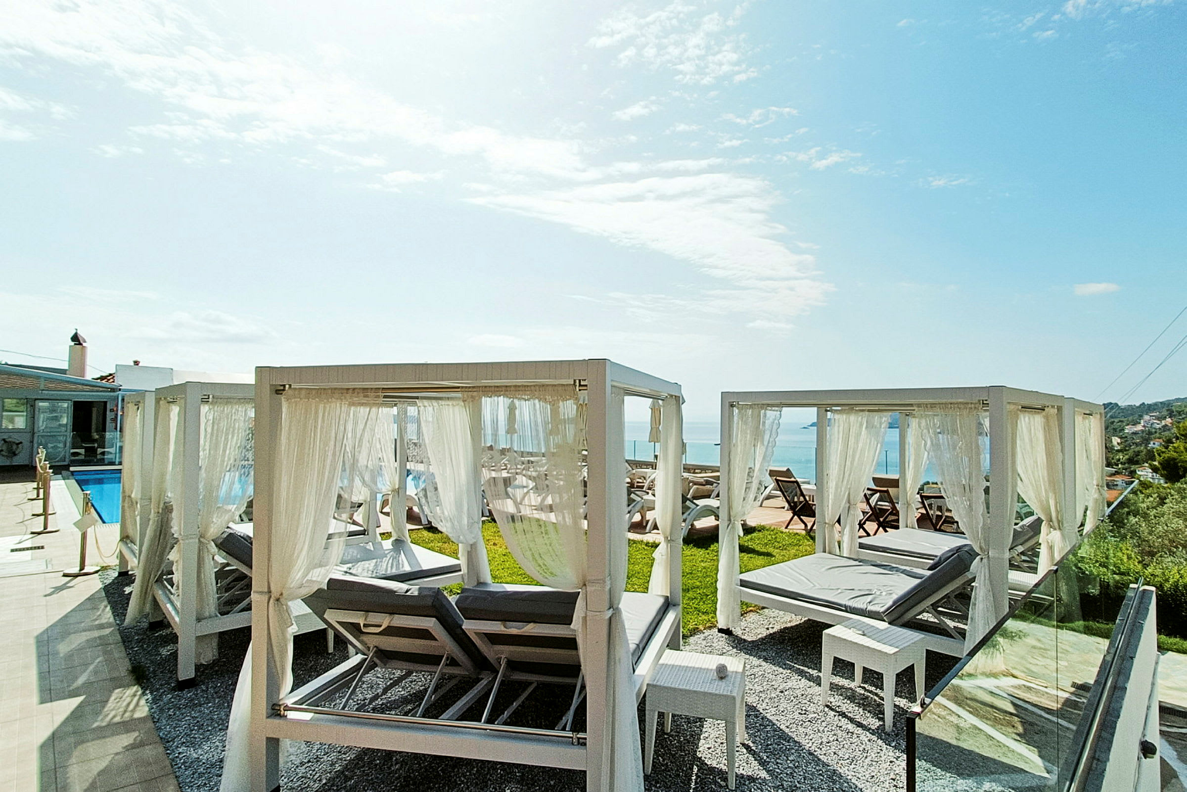 Solstolar med vita baldakiner vid en pool och utsikt mot havet. (AI-genererad text)