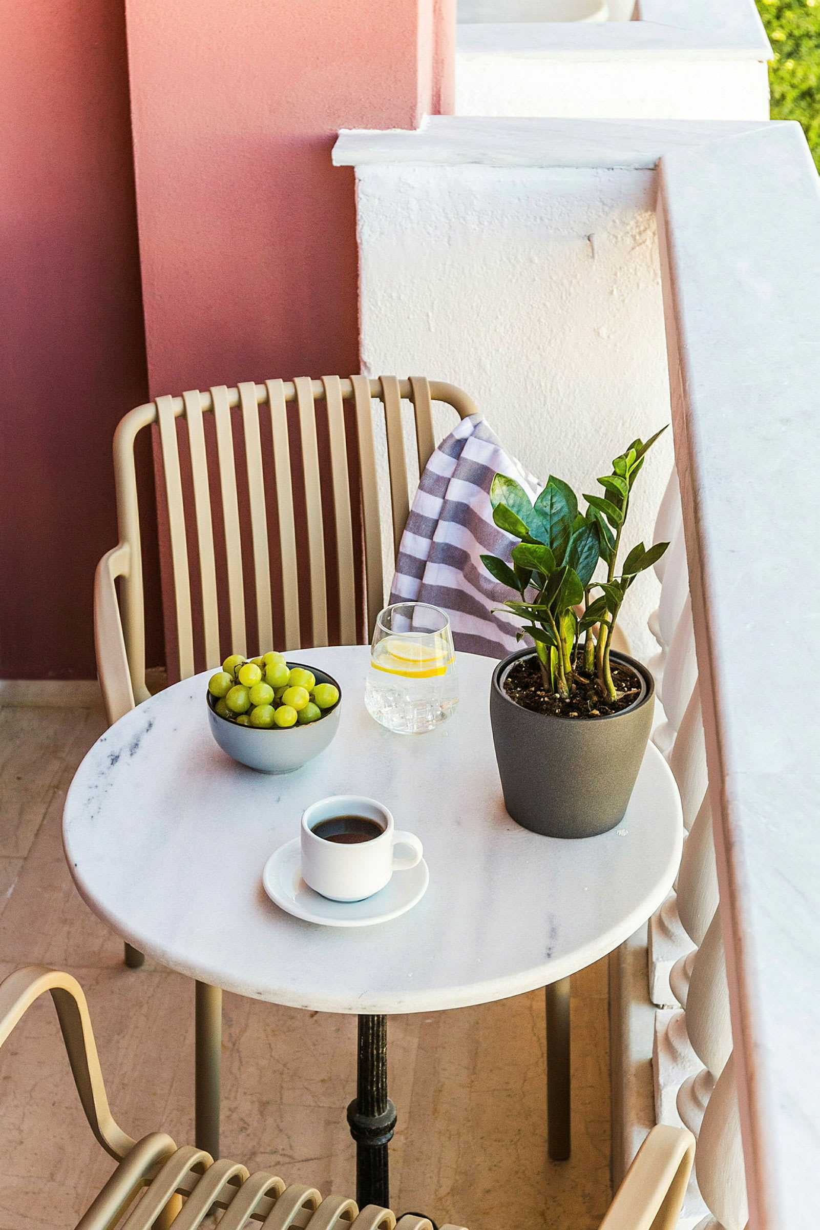 En balkong med ett bord med en kaffekopp, ett glas vatten, en skål med vindruvor och en grön växt. (AI-genererad text)