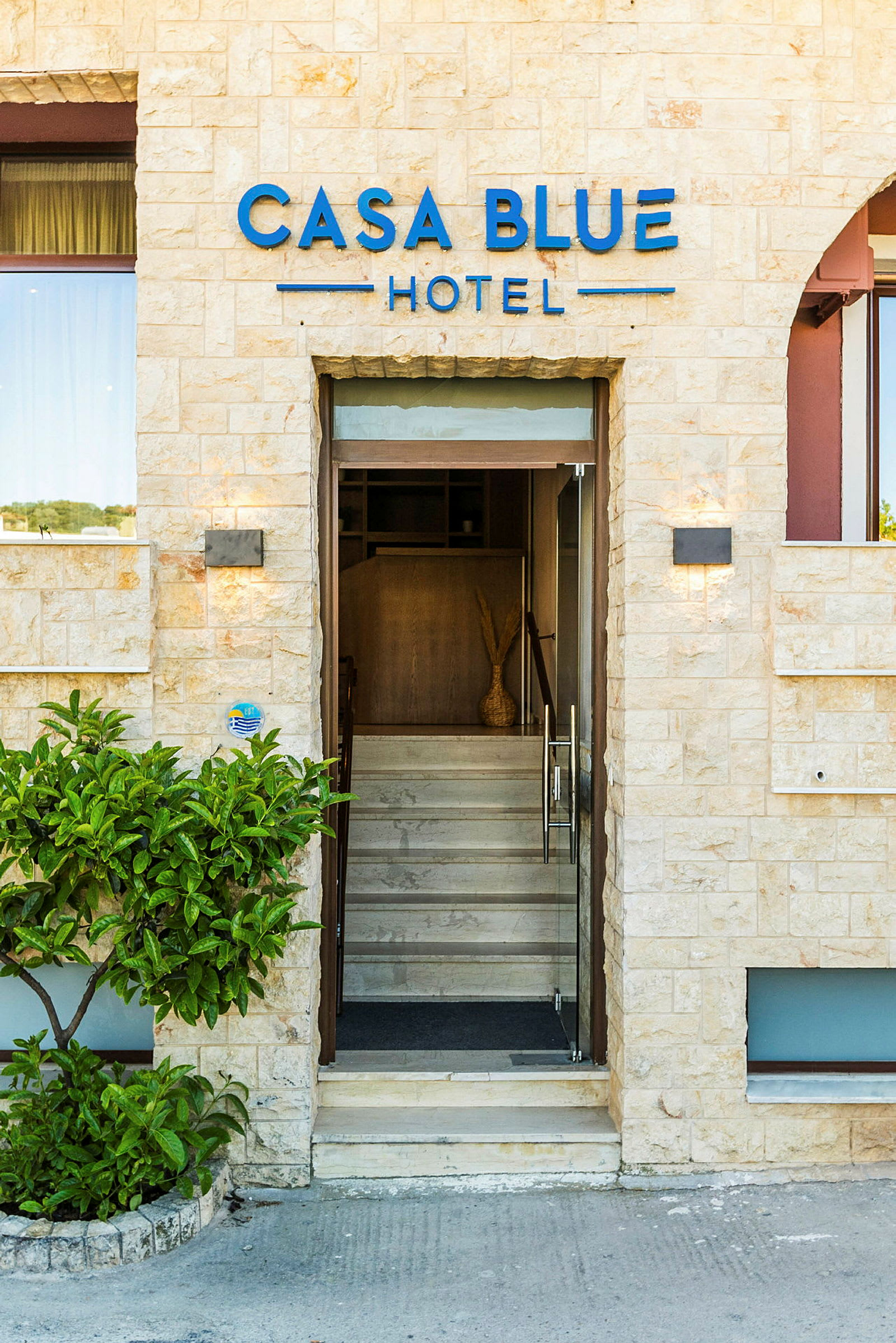 Entrén till Casa Blue Hotel, med glasdörrar och stenfasad. (AI-genererad text)