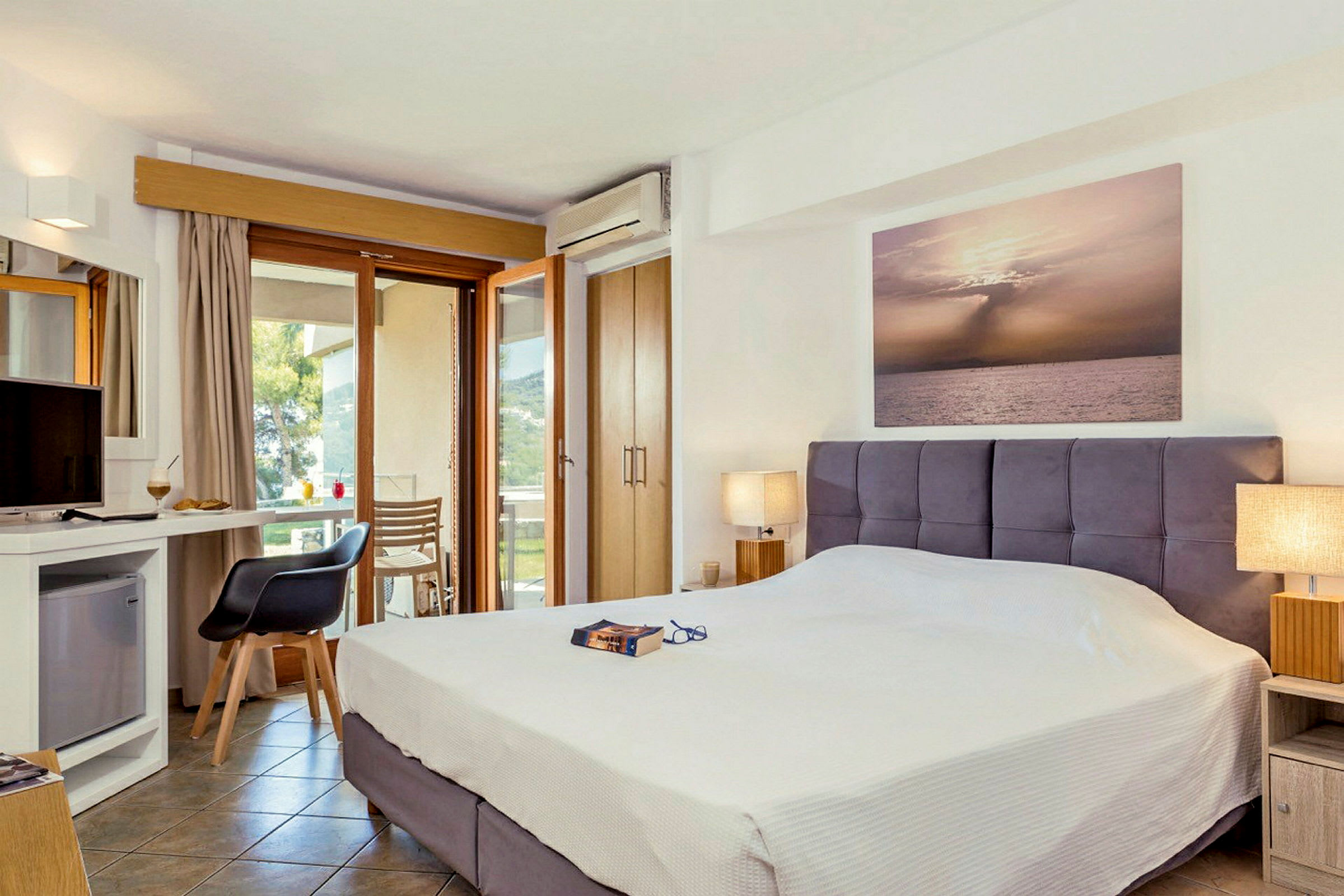 Ett hotellrum med en dubbelsäng, skrivbord och utsikt genom glasdörrar. (AI-genererad text)