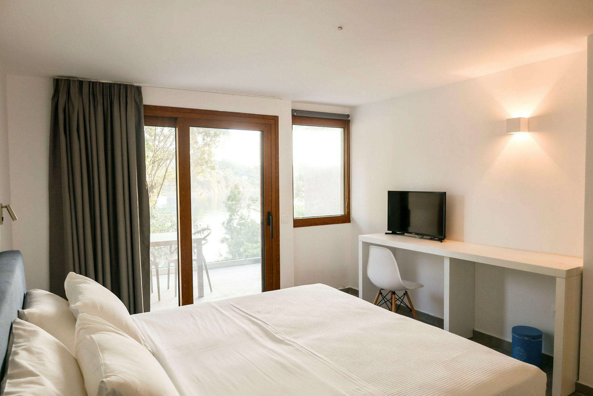 Ett hotellrum med en säng, skrivbord och stol samt balkong med utsikt. (AI-genererad text)