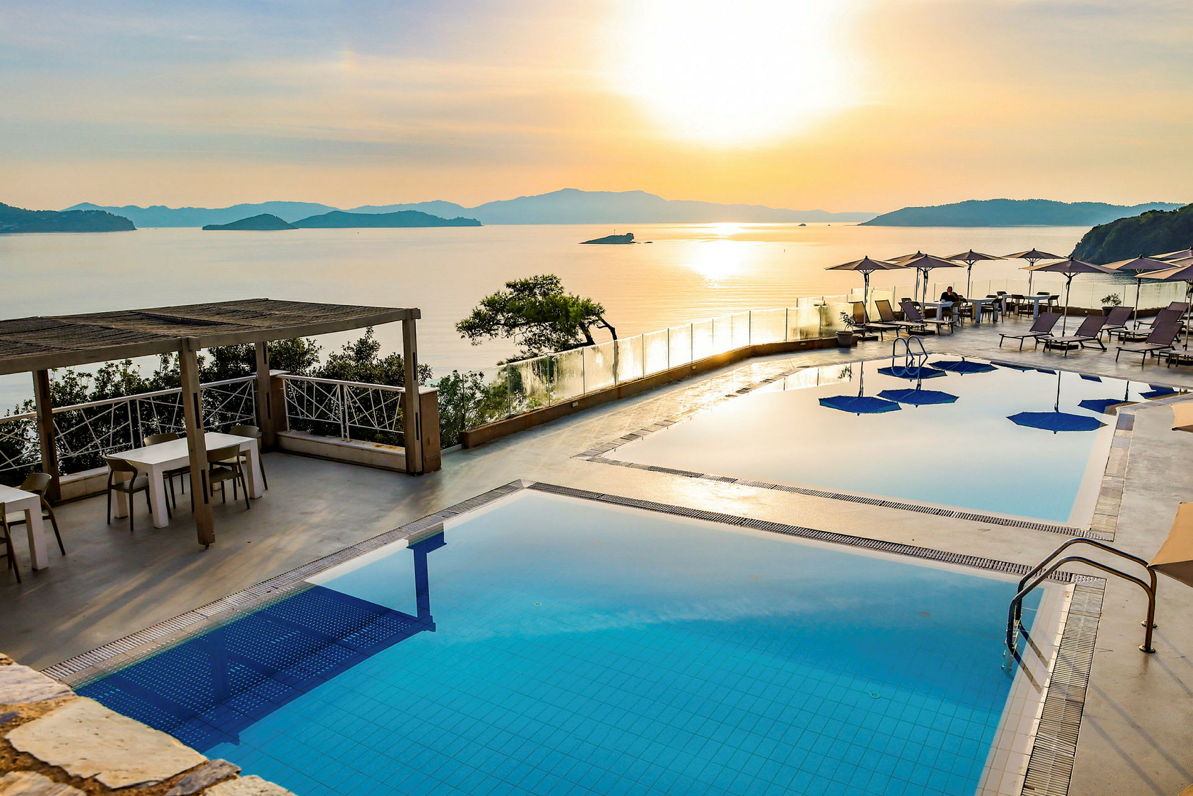 En poolterrass med utsikt över havet och solnedgången. (AI-genererad text)