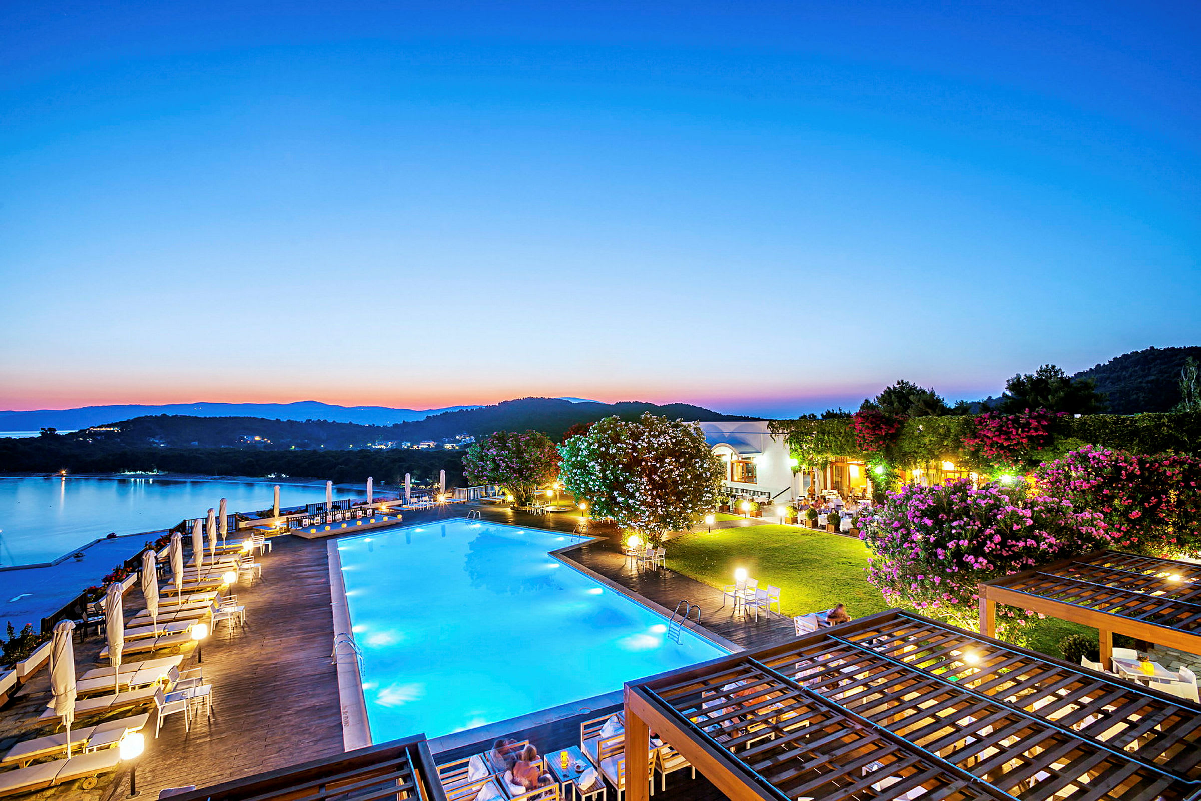 En pool vid en resort med utsikt över en stilla sjö och omgivande kullar i skymning. (AI-genererad text)