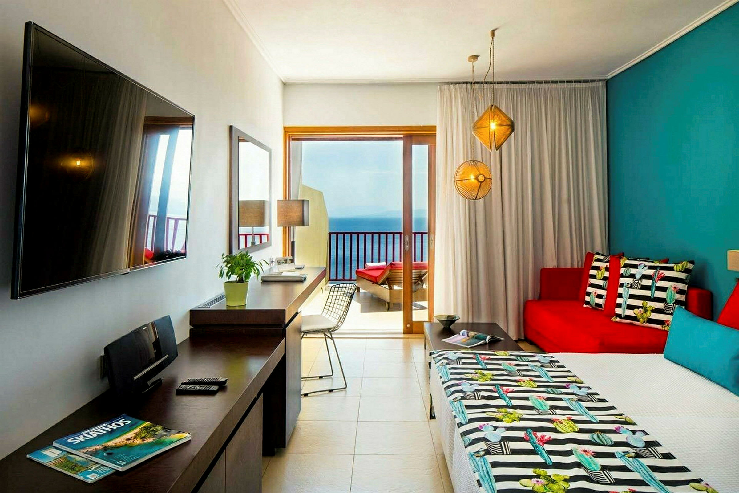 Ett hotellrum med en färgglad inredning, en säng, soffa, bord och en balkongdörr som vetter mot havet. (AI-genererad text)