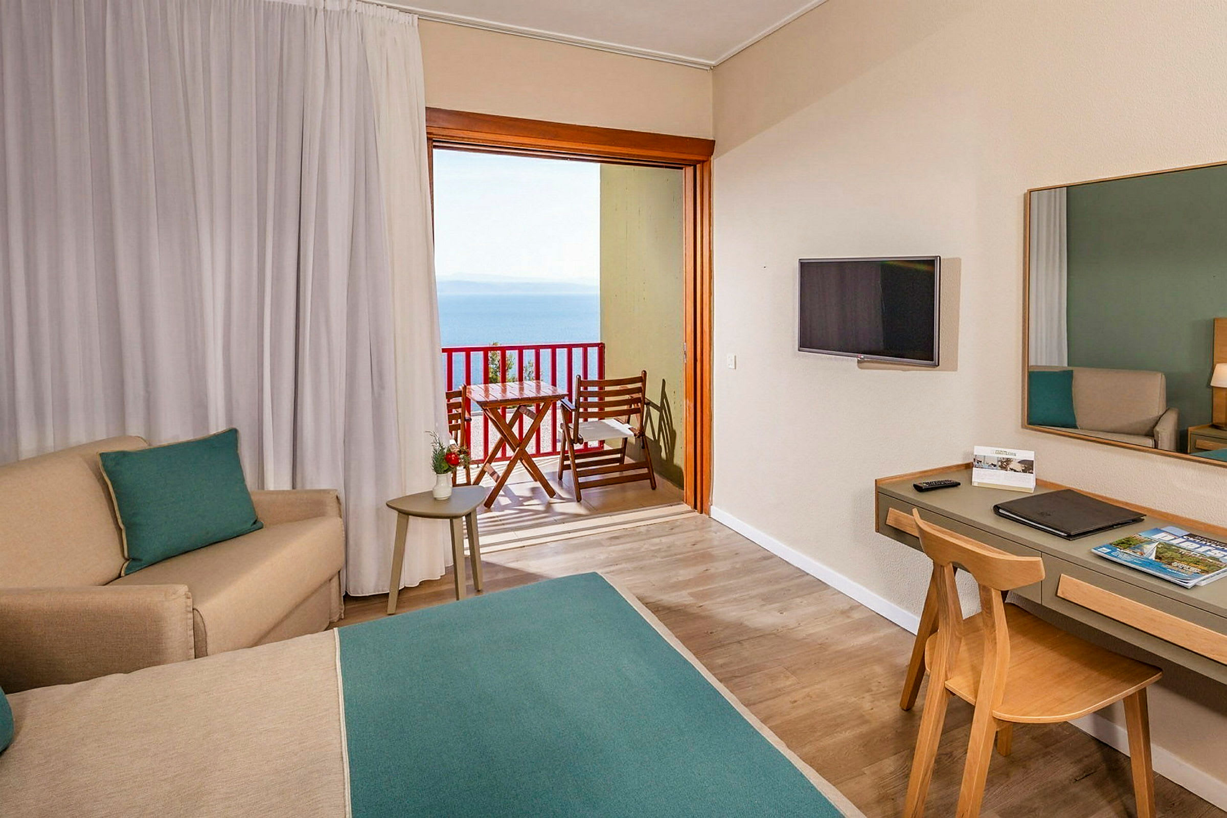 Ett hotellrum med sittgrupp, skrivbord och en balkong med havsutsikt. (AI-genererad text)