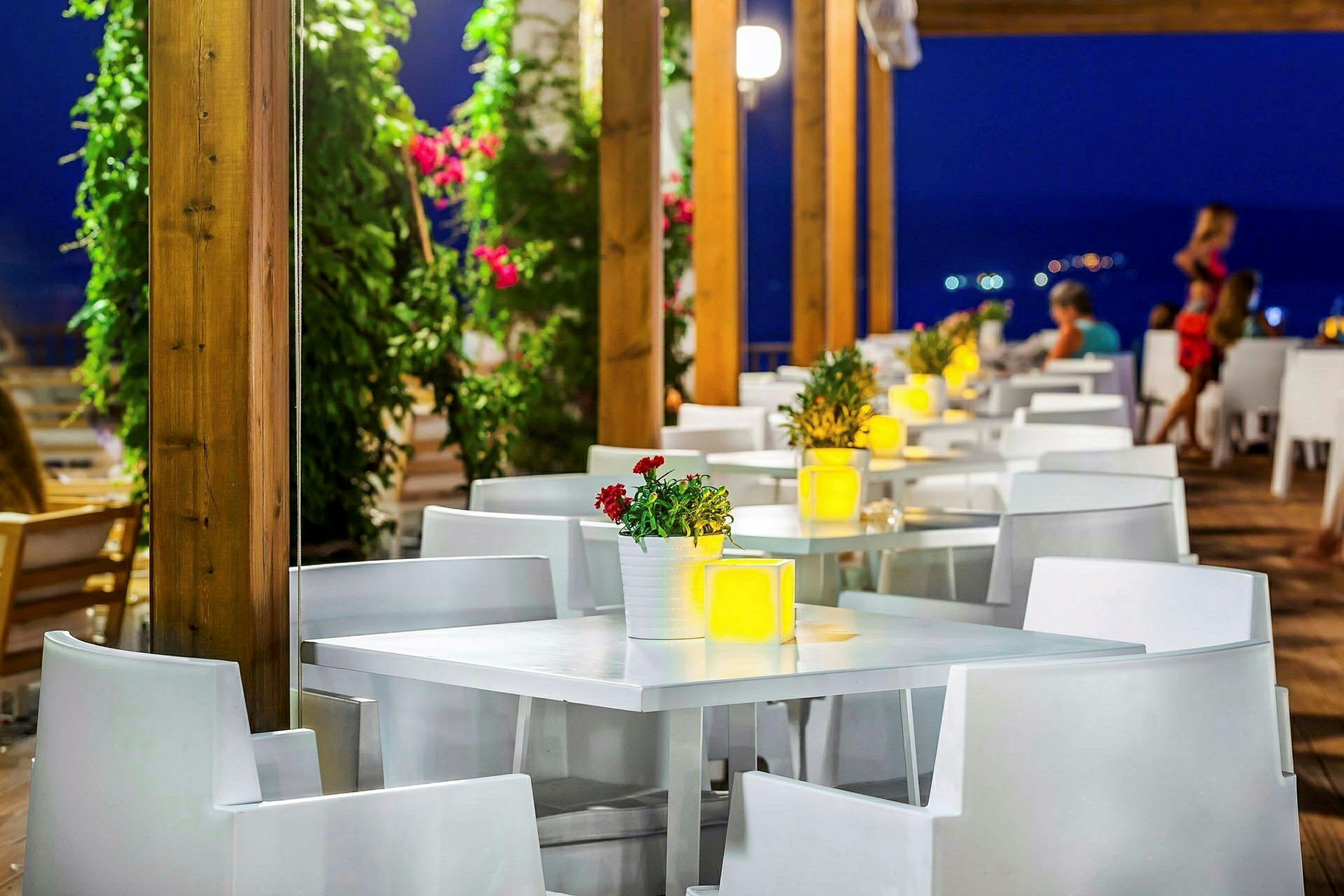 En utomhusrestaurang med vita bord och stolar, dekorerade med blommor och ljus på kvällen. (AI-genererad text)