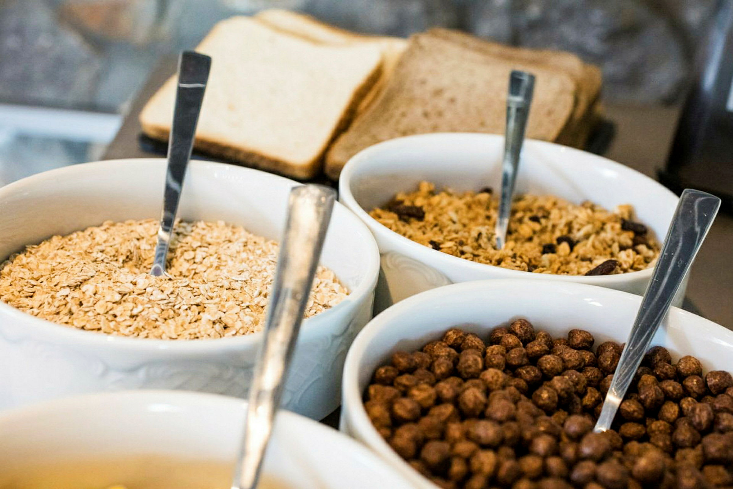 Skålar med olika typer av frukostflingor och bröd i bakgrunden. (AI-genererad text)