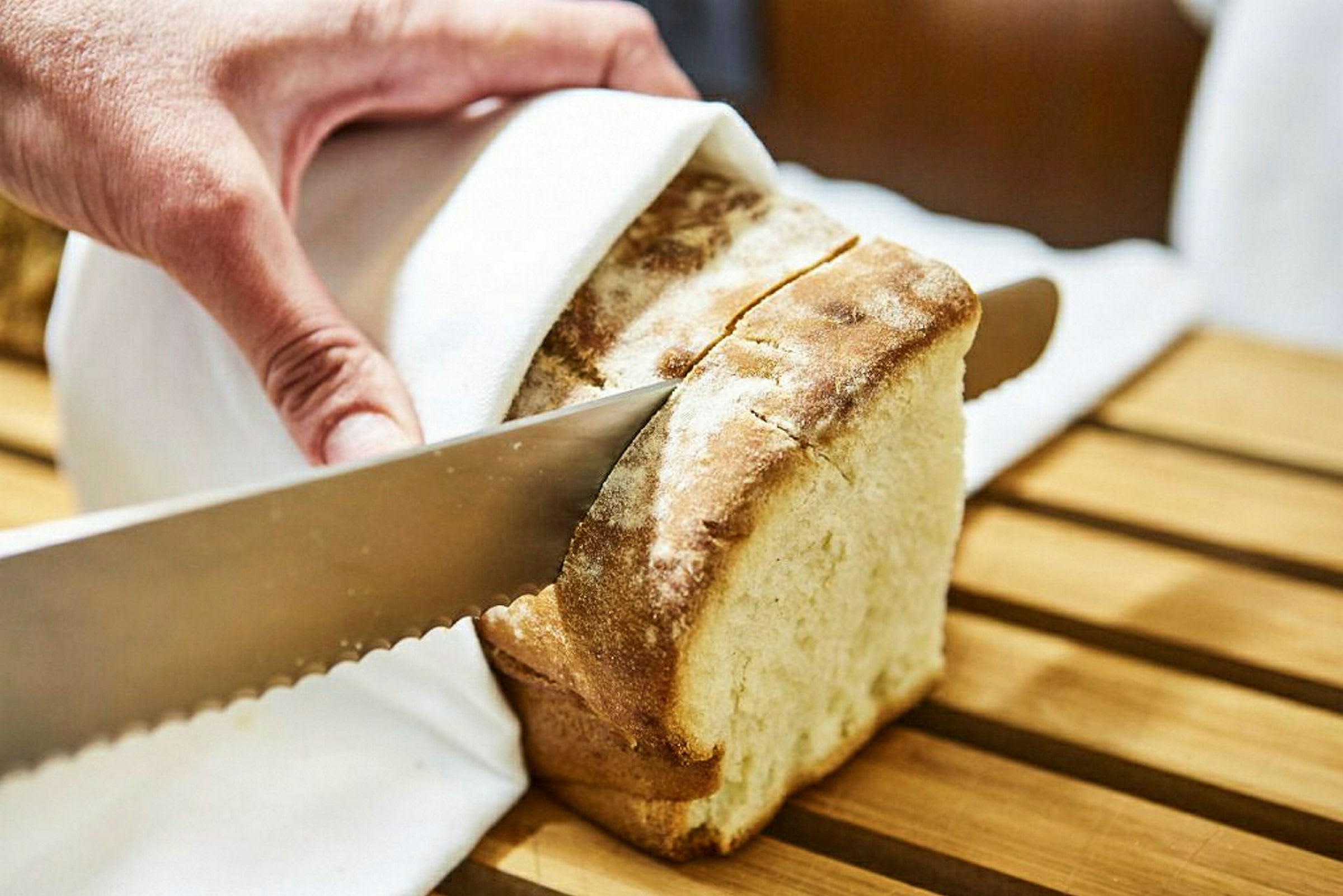 En hand skär en brödskiva med en tandad kniv. (AI-genererad text)