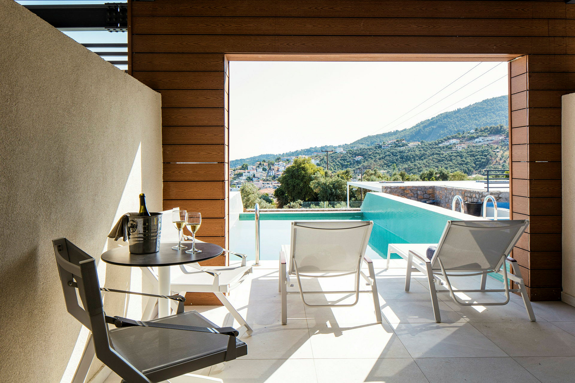 Terrass med utsikt över poolen och landskapet, med två solstolar och ett bord med en flaska och två glas. (AI-genererad text)