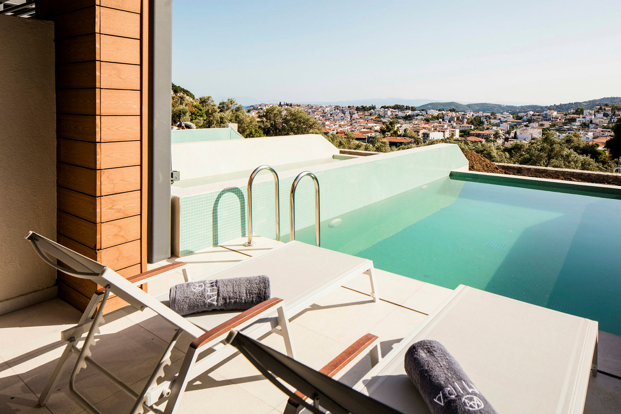 Terrass med solstolar och en pool, med utsikt över en stad. (AI-genererad text)