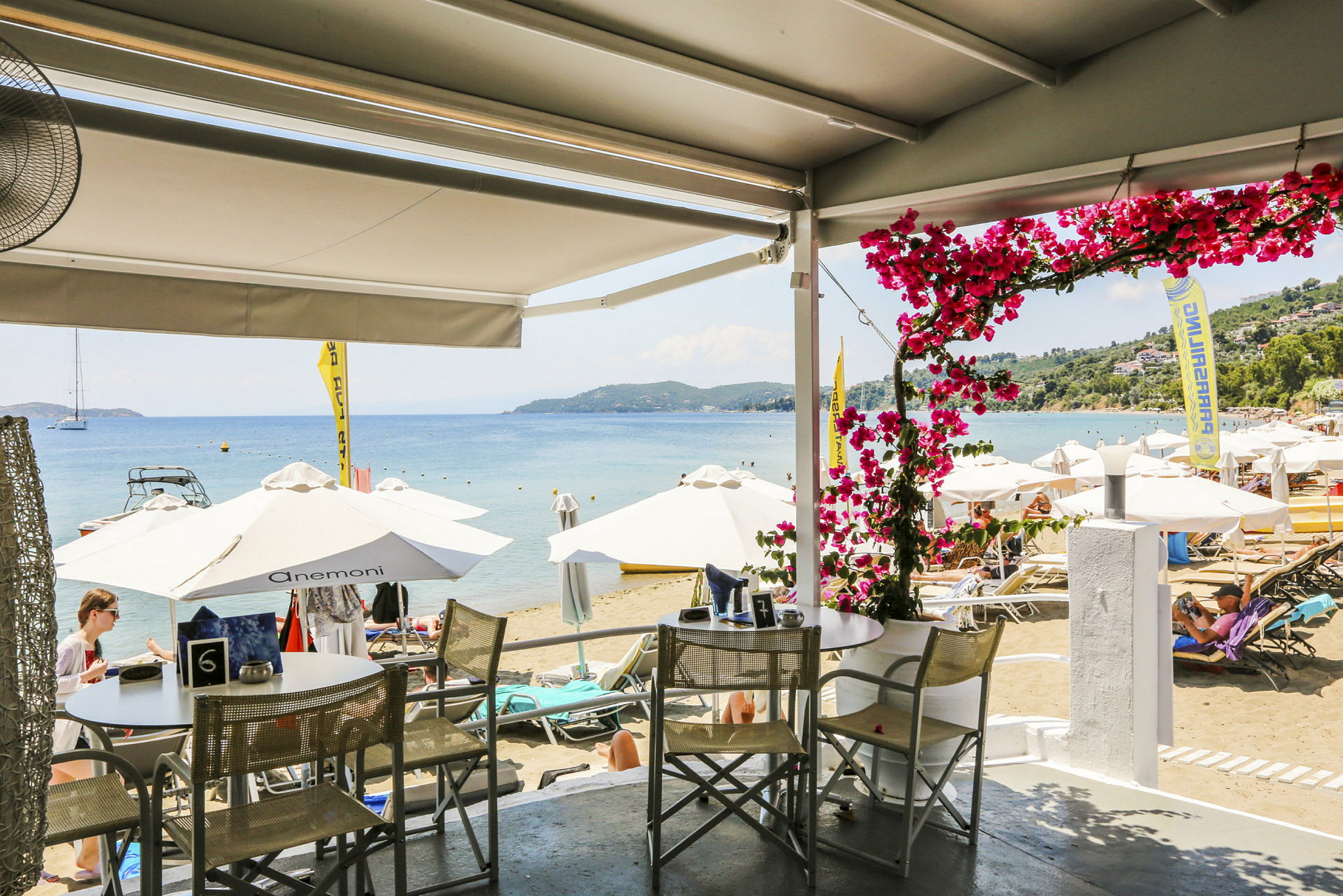 Vy från en restaurang med utsikt över en strand med parasoller och solstolar vid havet. (AI-genererad text)